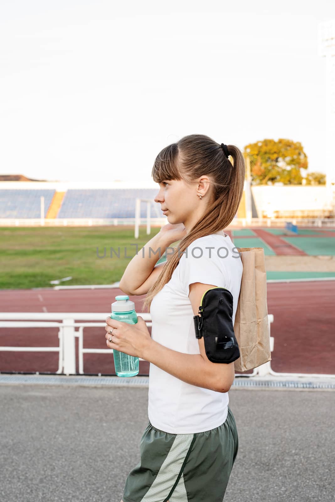 Teenager girl walking at the stadium with the papper bag after workout