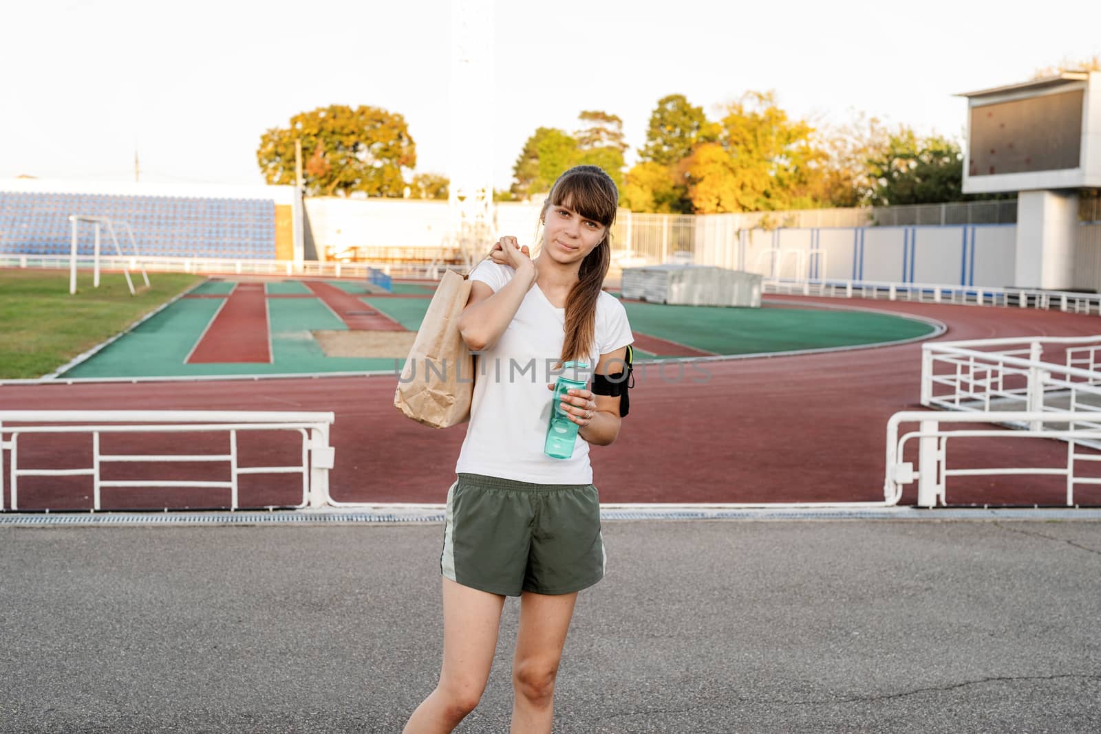 Teenager girl walking at the stadium with the papper bag after workout