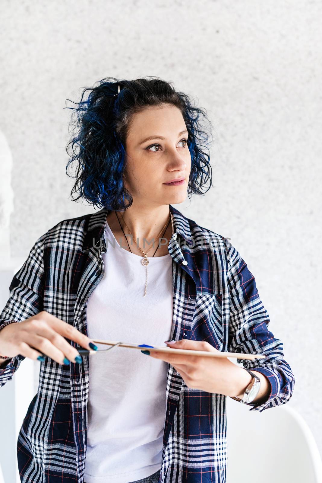 Creative woman with blue dyed hair painting in her studio by Desperada