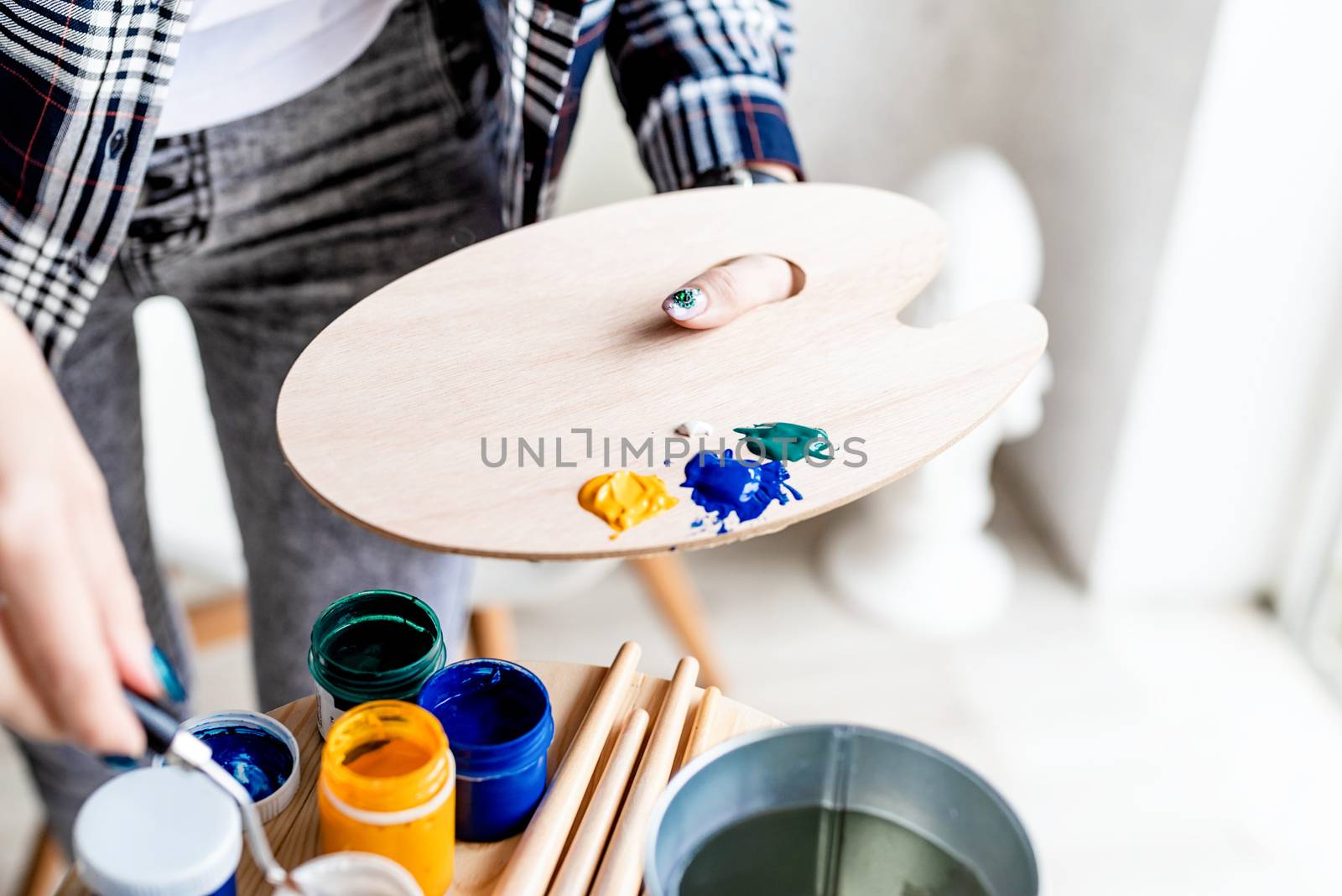 Close up of woman artist hands mixing colors on wooden art palette by Desperada