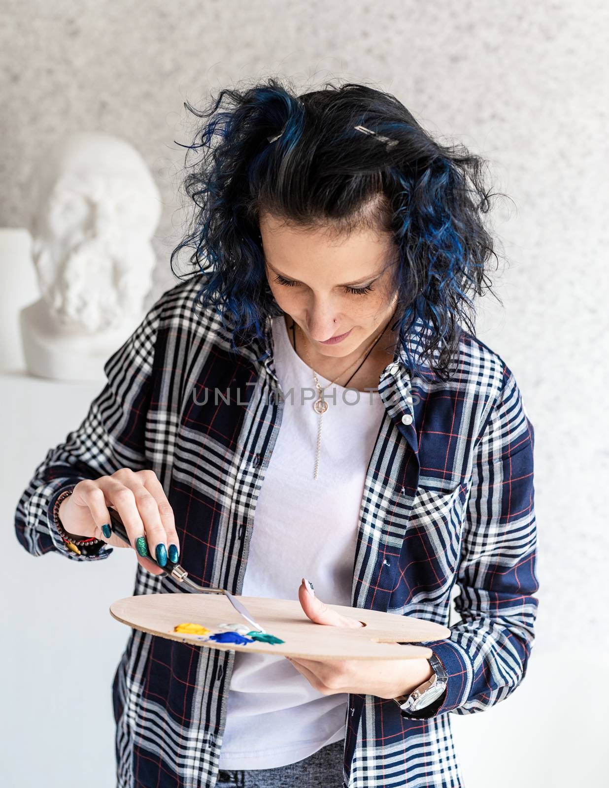 Creative woman with blue dyed hair painting in her studio by Desperada