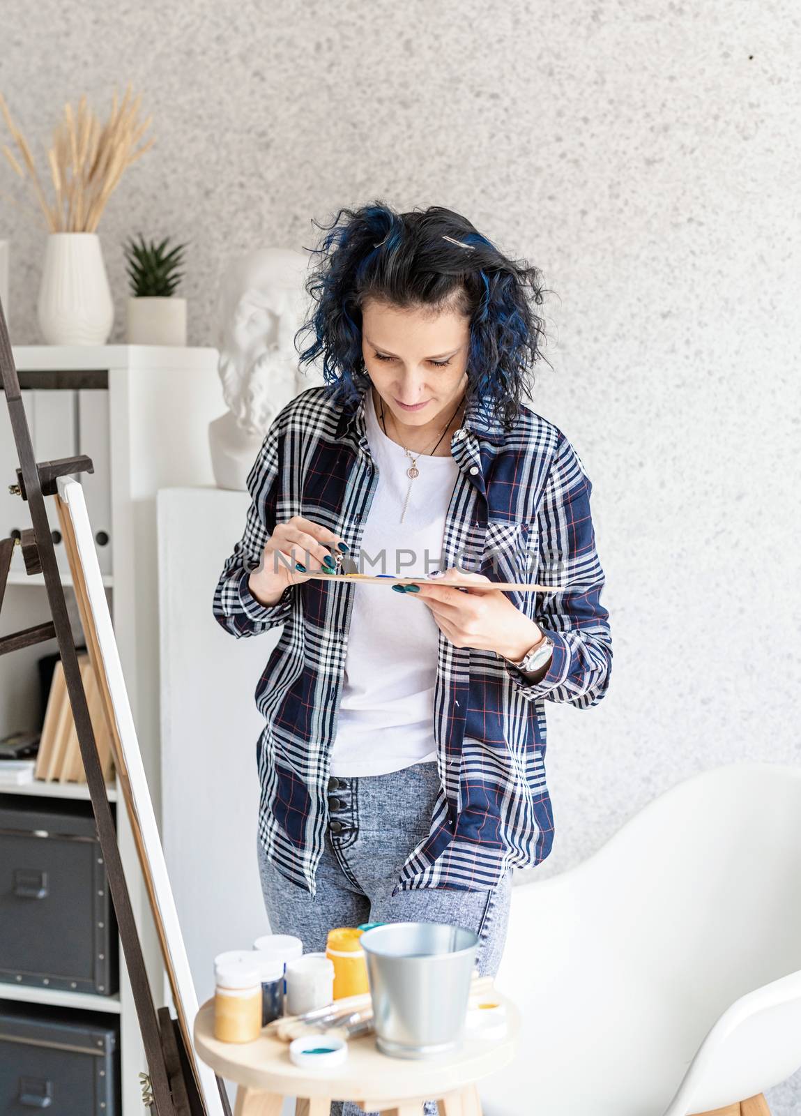 Creative woman with blue dyed hair painting in her studio by Desperada