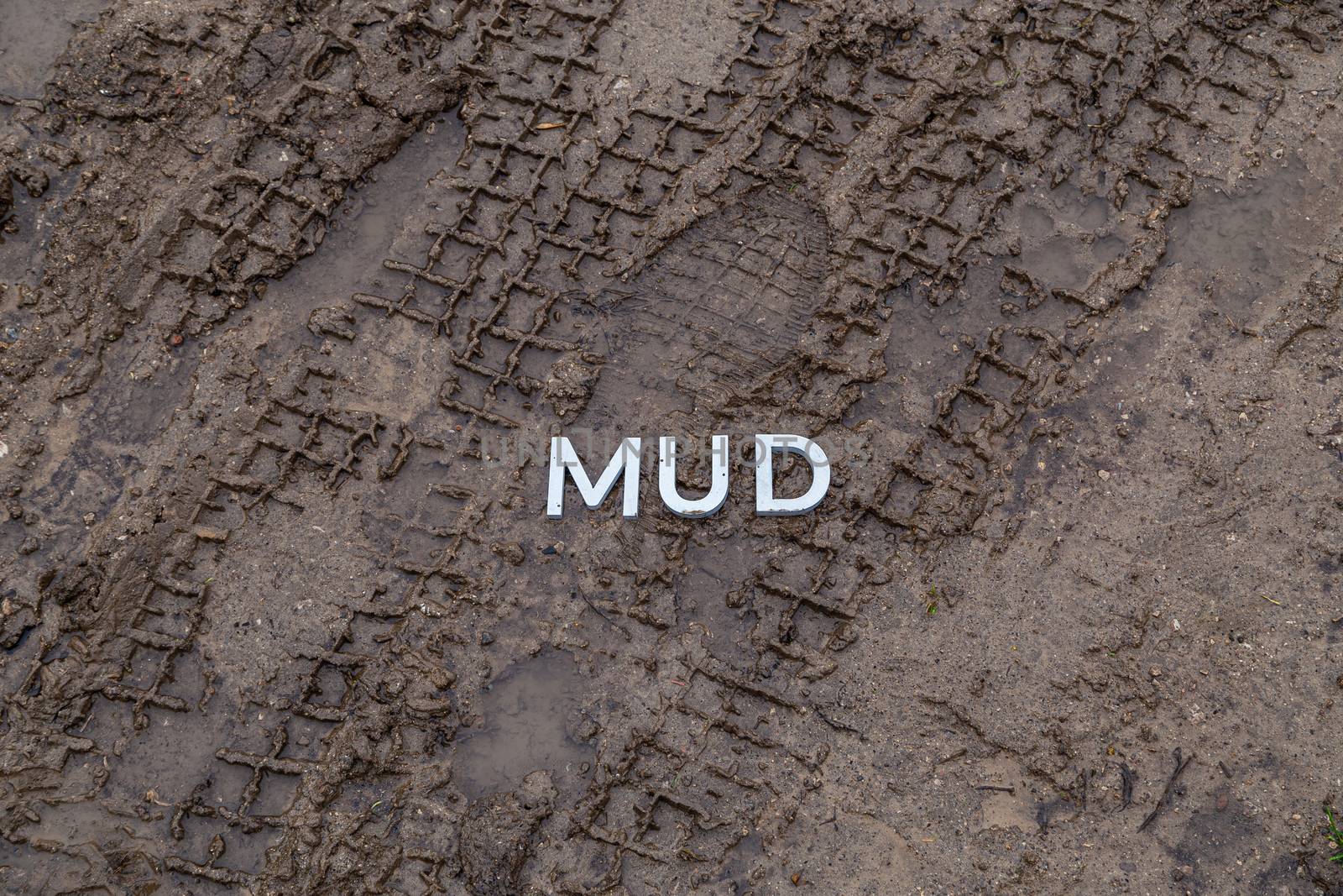 the word mud laid with silver metal letters on wet dirt surface with directly above perspective under cloudy autumn day light