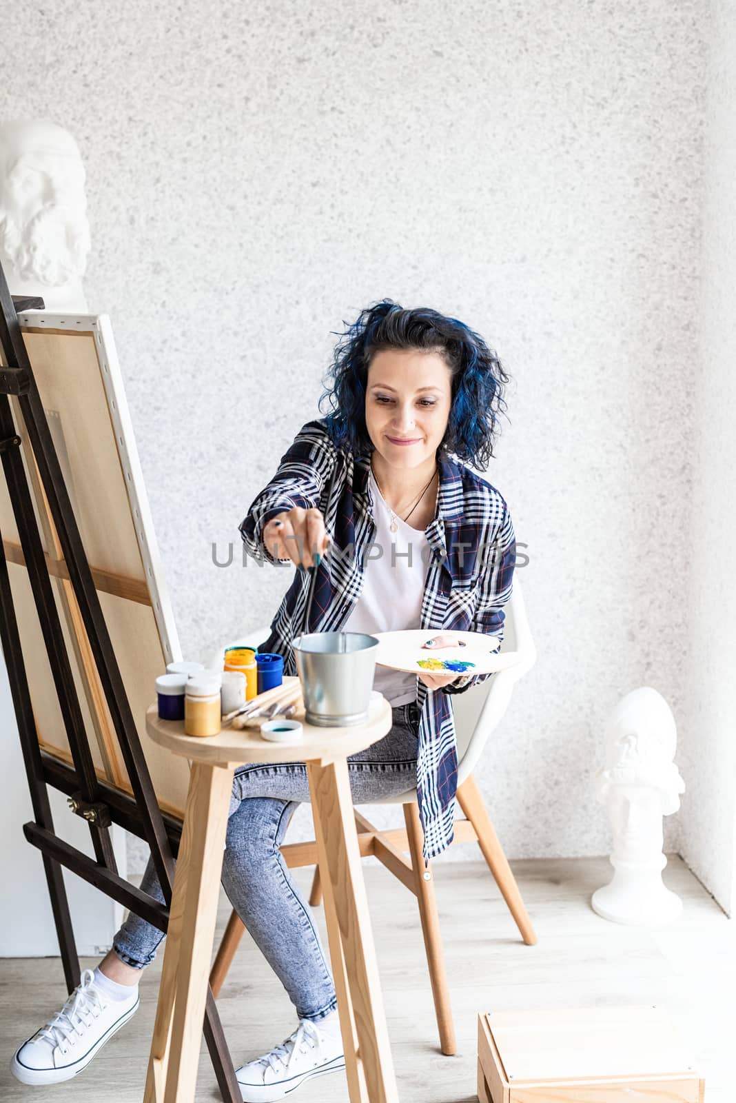 Creative woman with blue dyed hair painting in her studio by Desperada