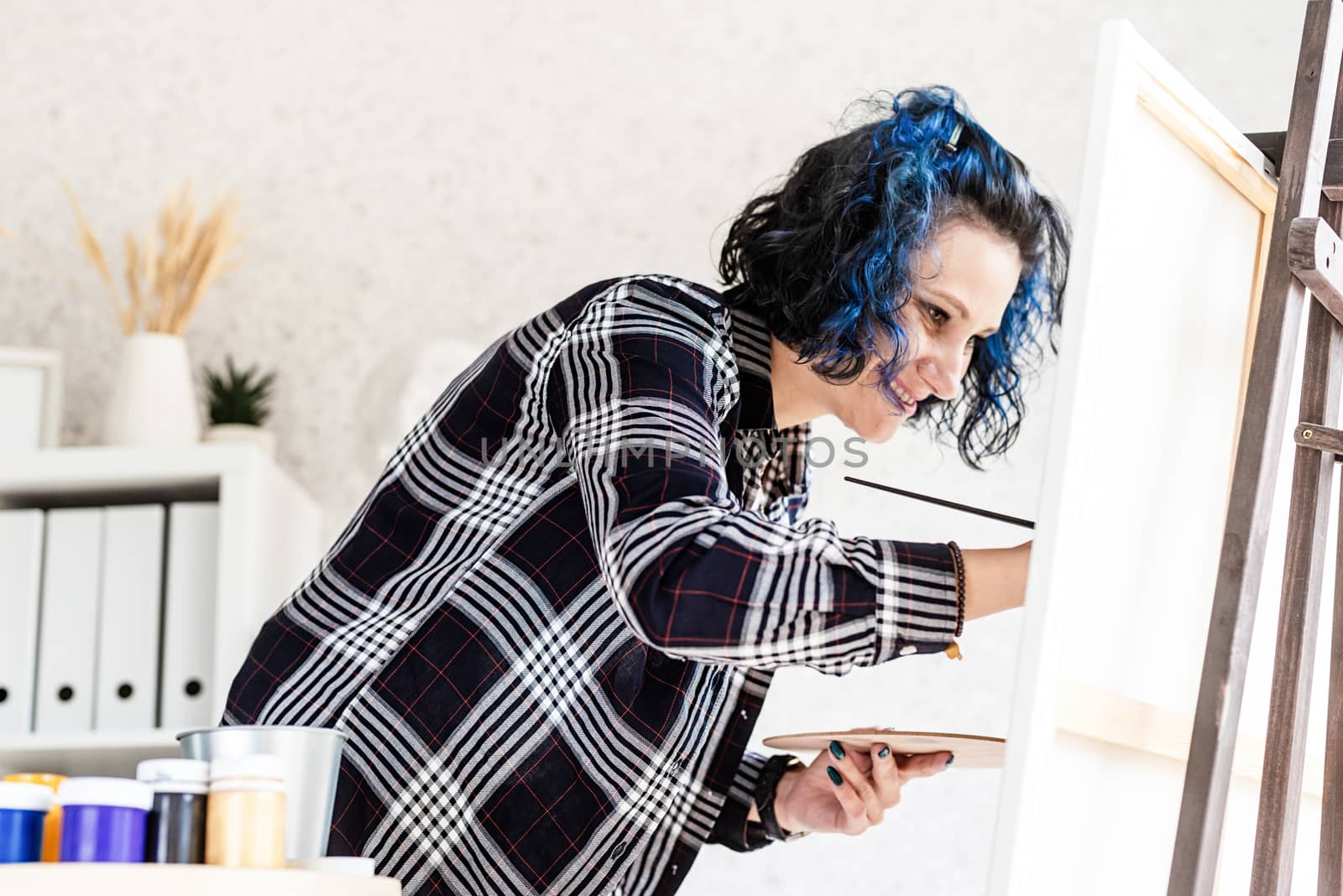 Creative woman with blue dyed hair painting in her studio by Desperada