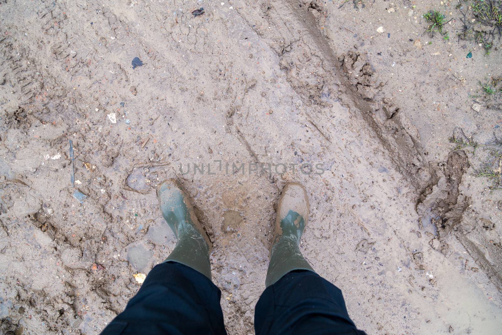 feet in green rubber boots stands on wet brown mud directly above view, directly above first person gonzo view