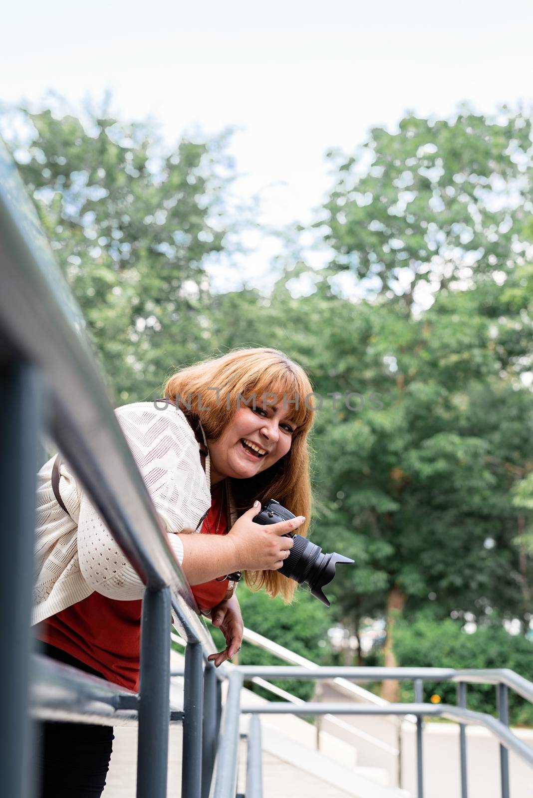 Plus size woman photographer outdoors holding a camera and laughing by Desperada