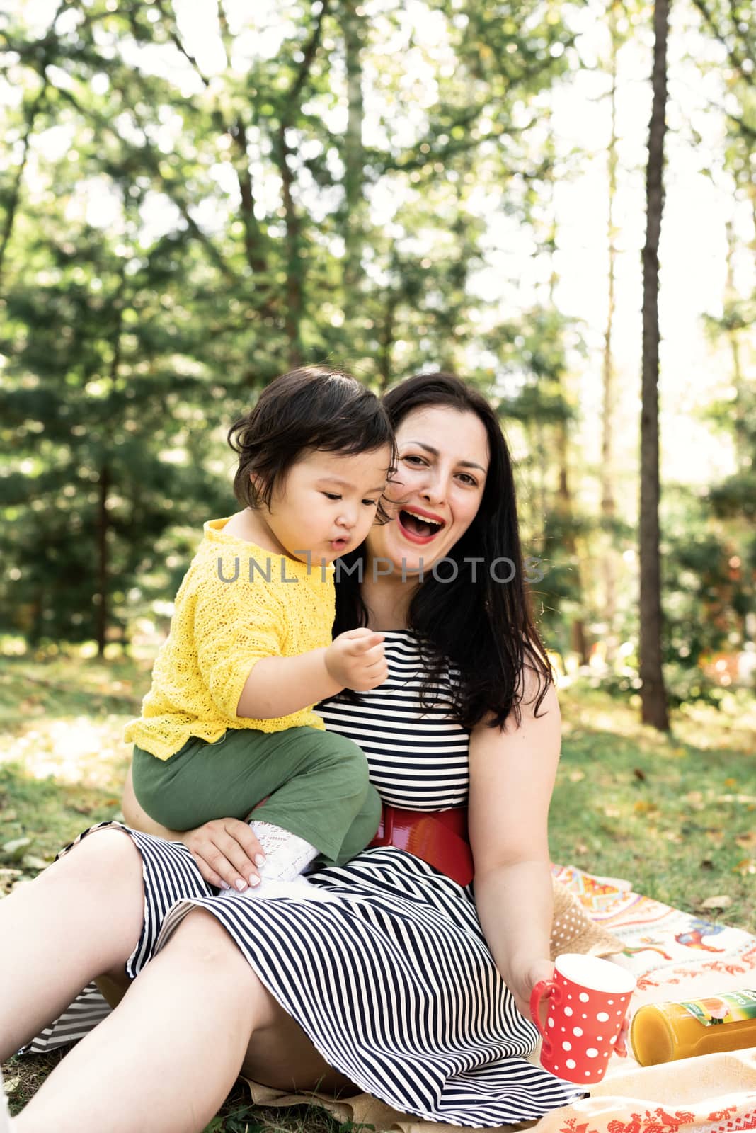 Happy multiracial family of mother and daughter in the park on a picnic by Desperada