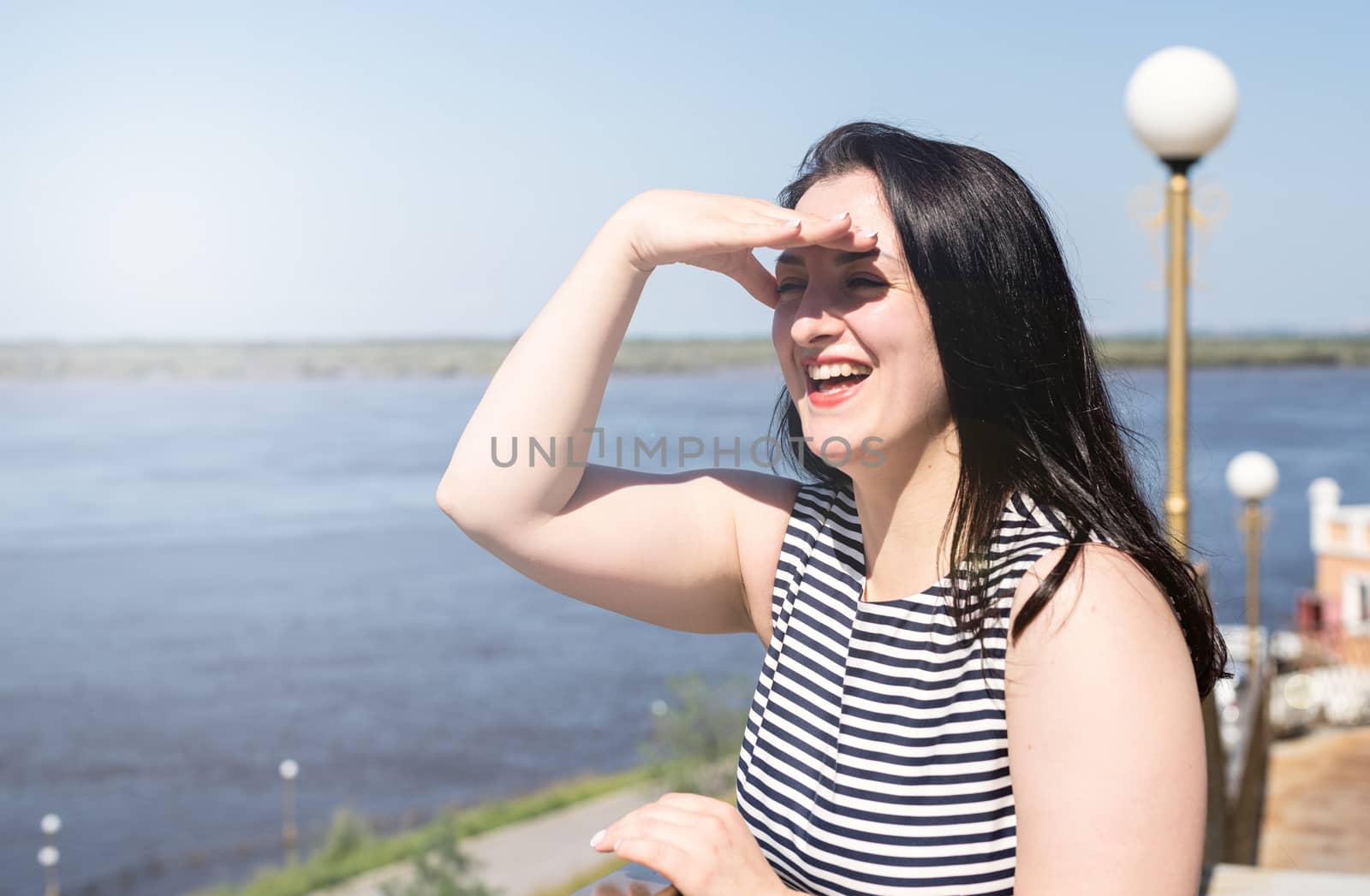 Happiness concept. Young laughing woman standing by the riverside enjoying the view covering her eyes with her hand