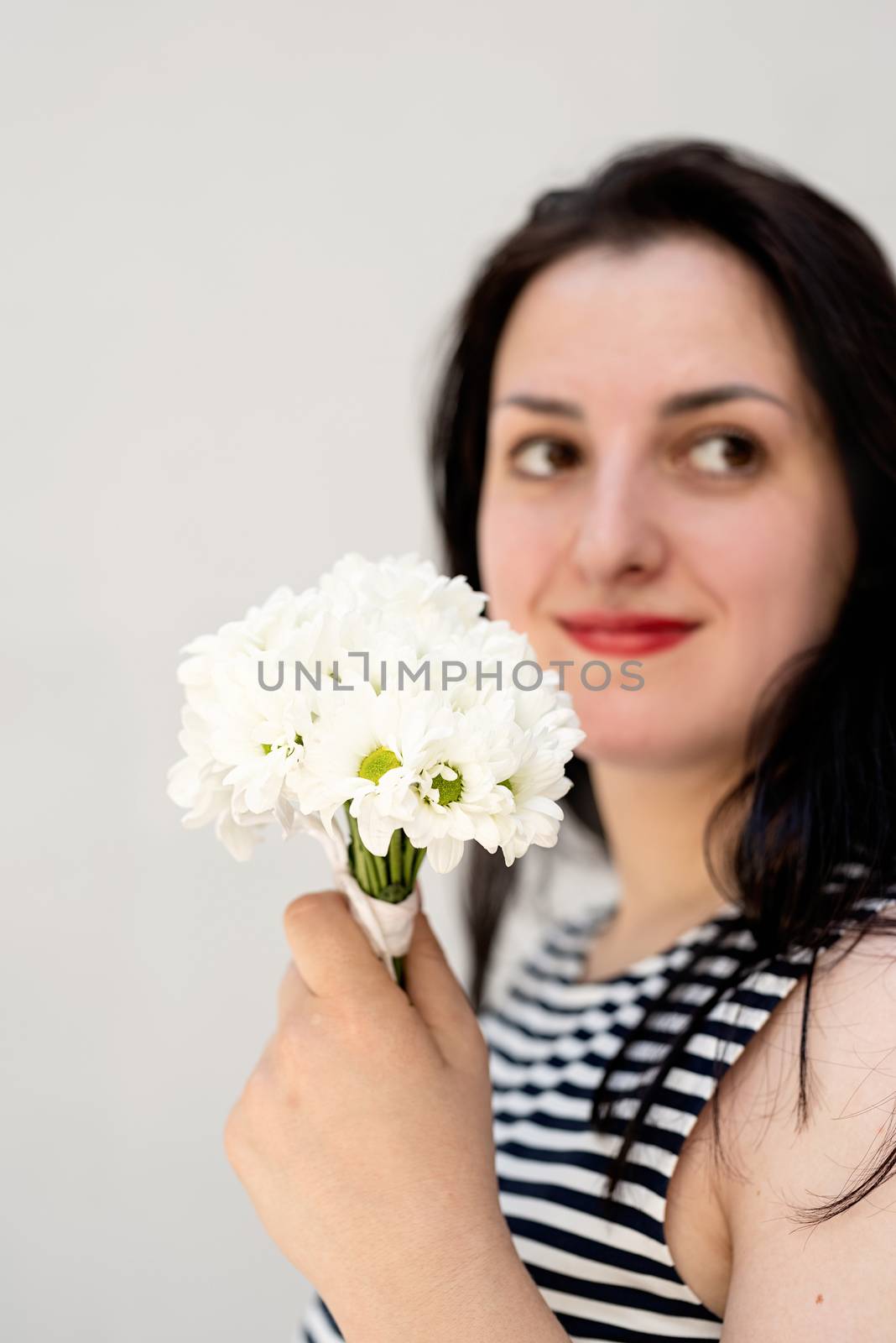 Happy young woman holding a bouquet of flowers on a gray solid background by Desperada