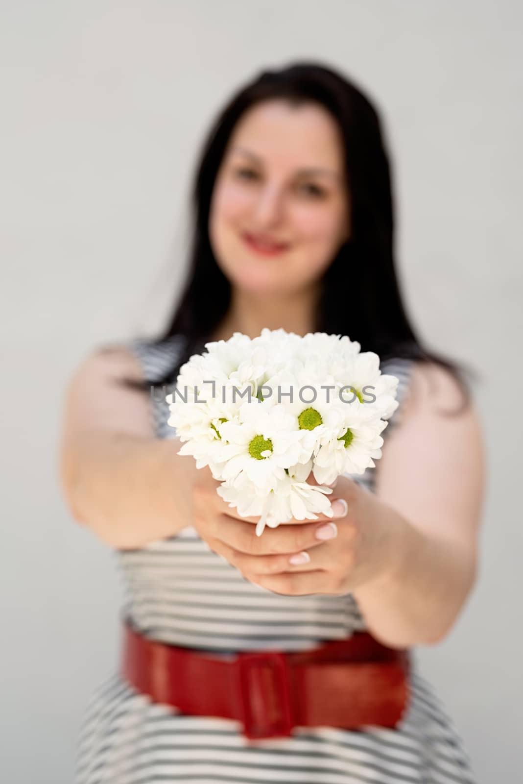 Happy young woman holding a bouquet of flowers on a gray solid background by Desperada