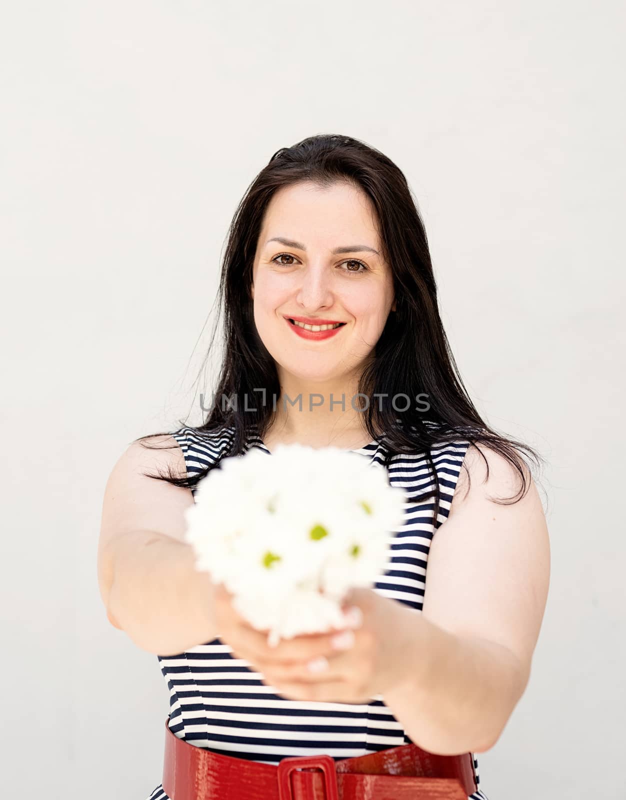 Happy young woman holding a bouquet of flowers on a gray solid background by Desperada