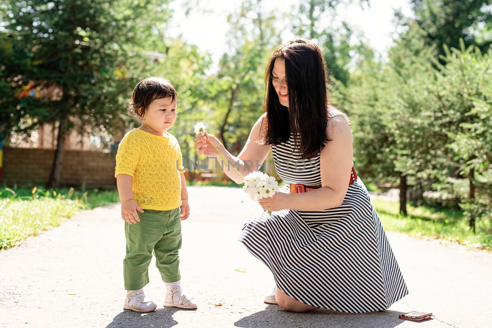 Mother walking her daughter in the park giving her flowers by Desperada