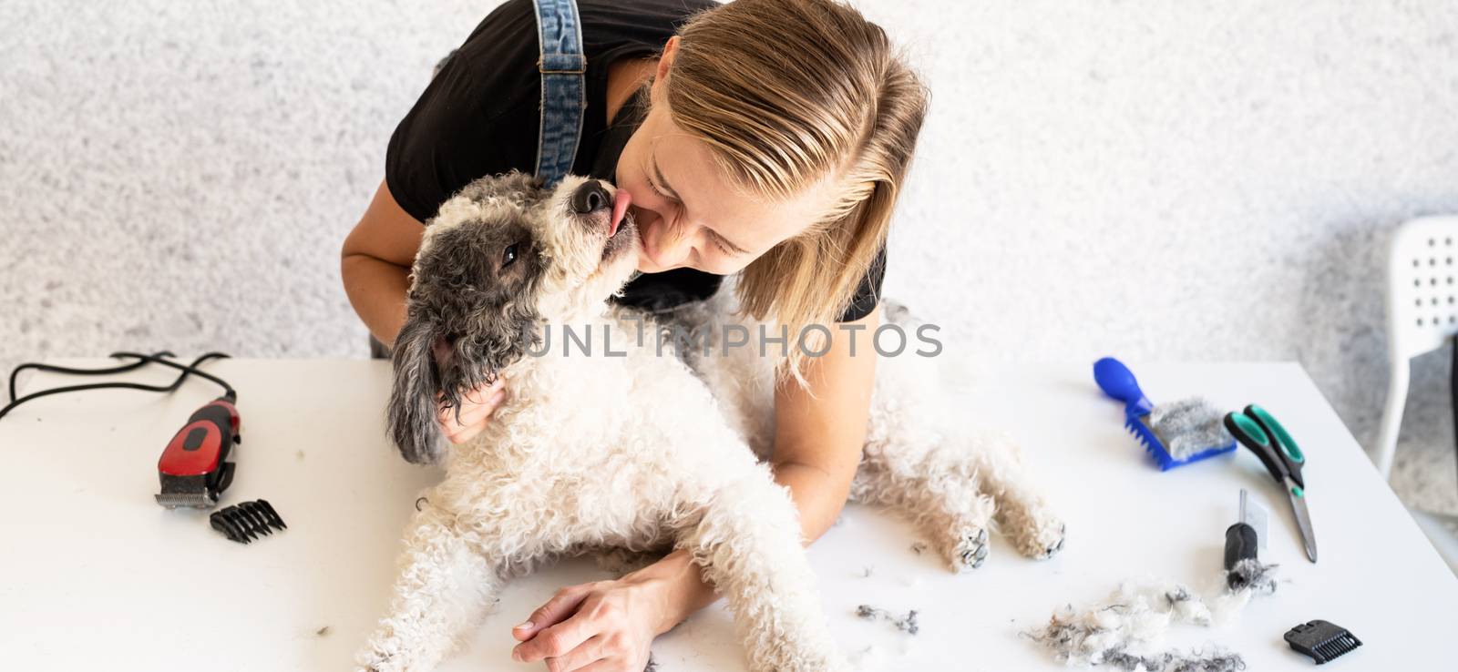 Blong young groomer hugging and kissing her dog by Desperada