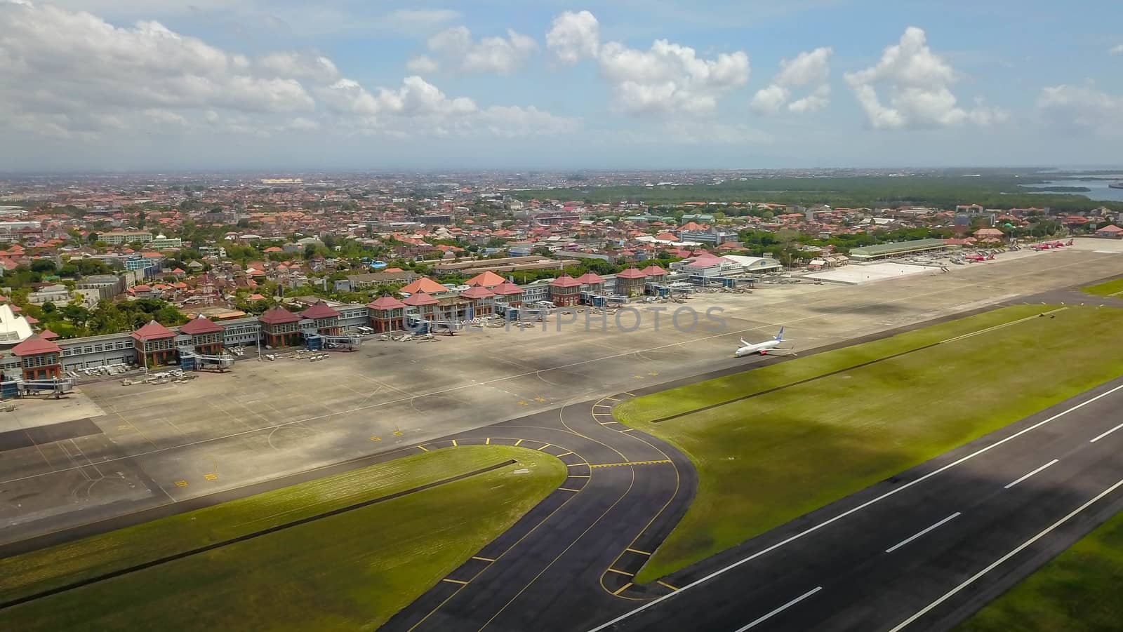 Airport - aerial view with runways, taxis, grass and air-crafts. Aerial view to Ngurah Rai airport. The plane goes down the runway.