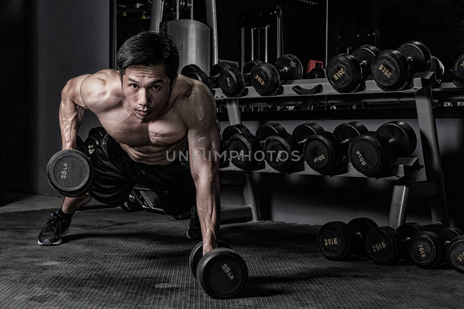Strong fitness man doing arm workout with dumbbells in the gym