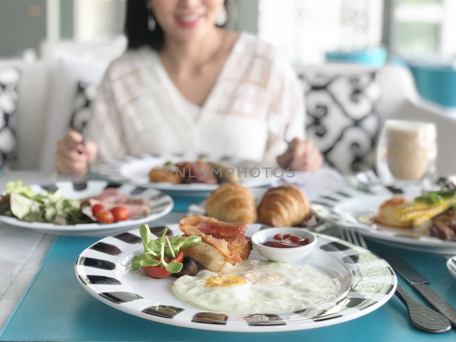 Young woman having healthy breakfast - fried egg, beans, salad, tomatoes, mushrooms, bacon and toast.