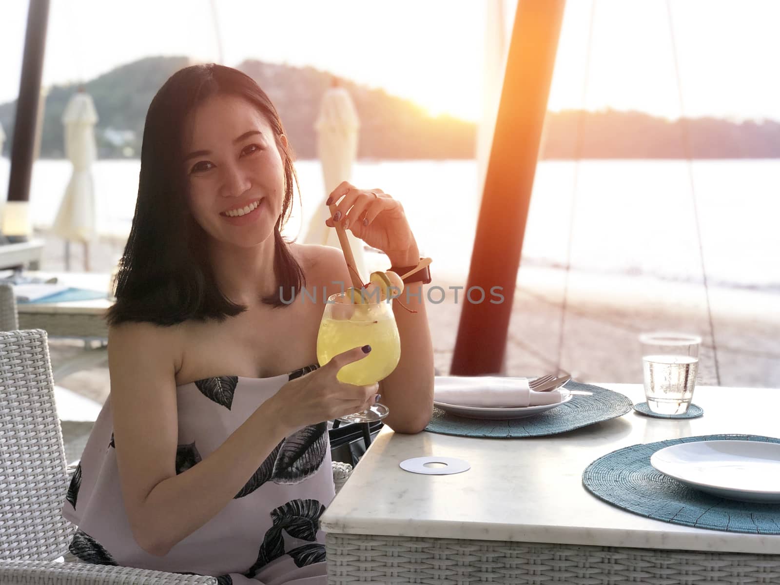 Beautiful woman holding a fruit cocktail on a tropical beach at sunset 