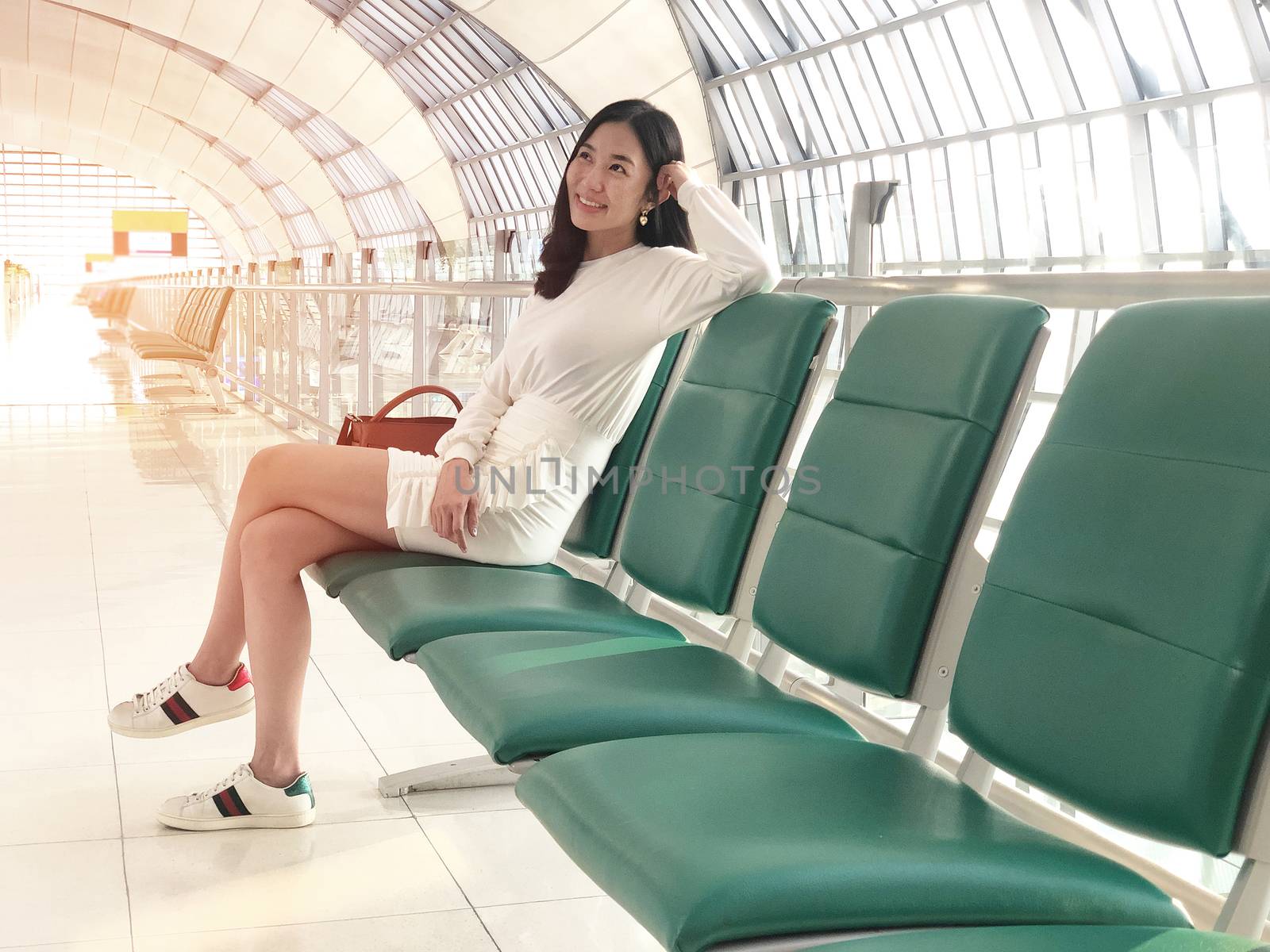 Young woman smiling with green chair sitting in airport hall while waiting landing