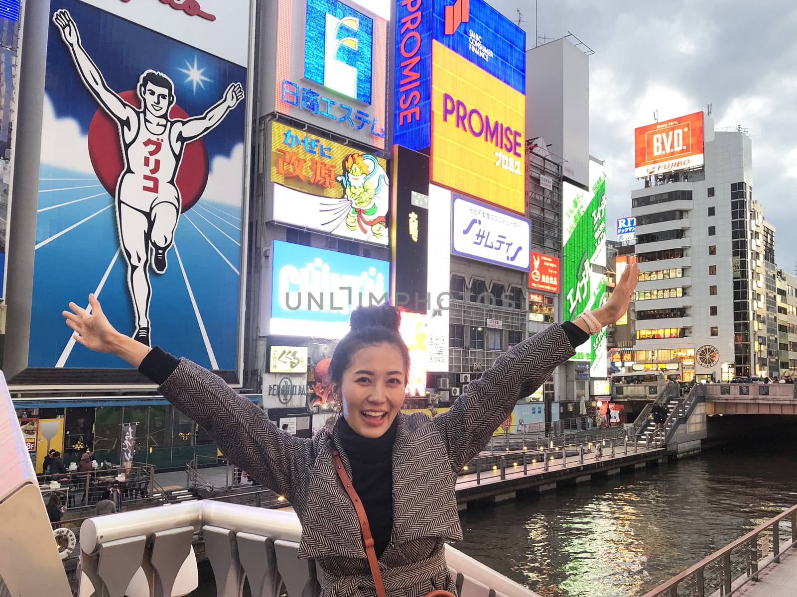 Osaka,Japan - Mar 26, 2019 : A young tourist woman tried to take the same pose as the Glico man neon signboard which is one of the most famous landmark Dontonbori in Namba Osaka,Japan. 