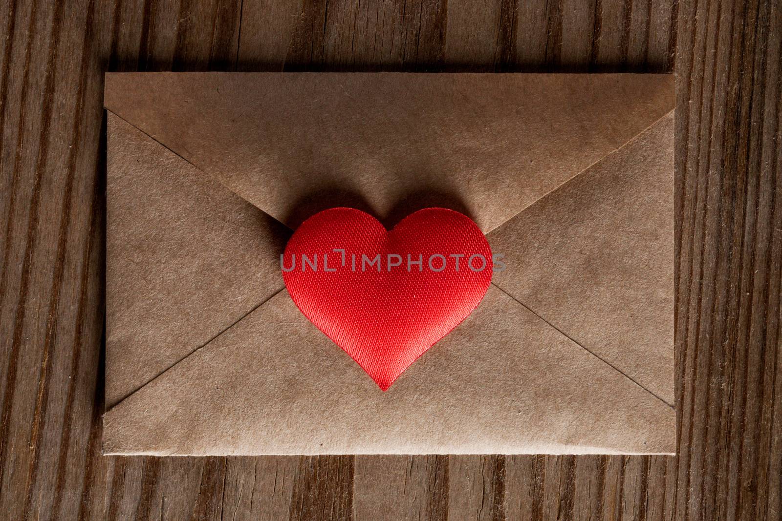 Valentine day love letter, envelope of craft paper with red heart on wooden background