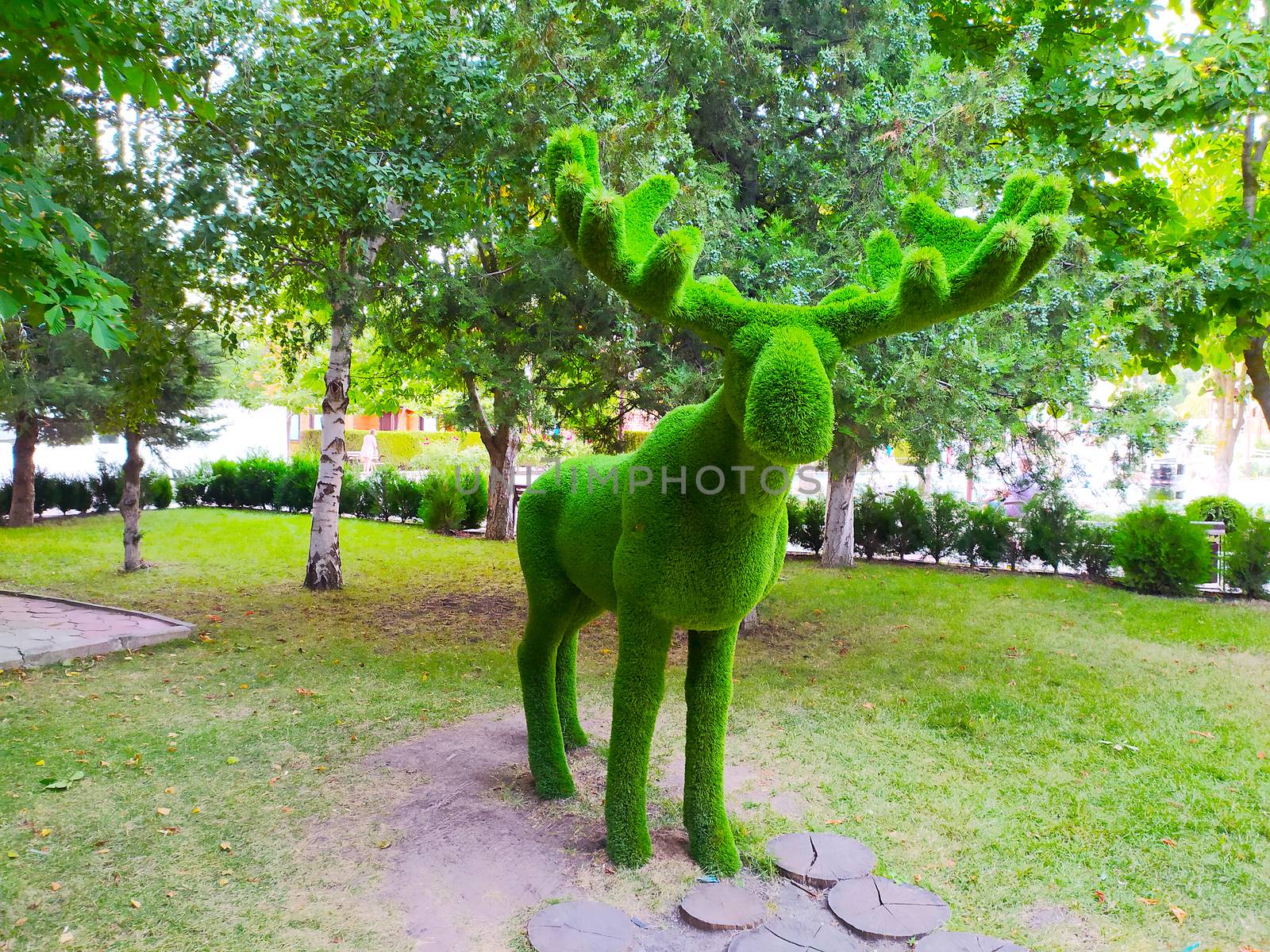 Sculpture of a deer with horns in a green Park against a background of trees. by Igor2006
