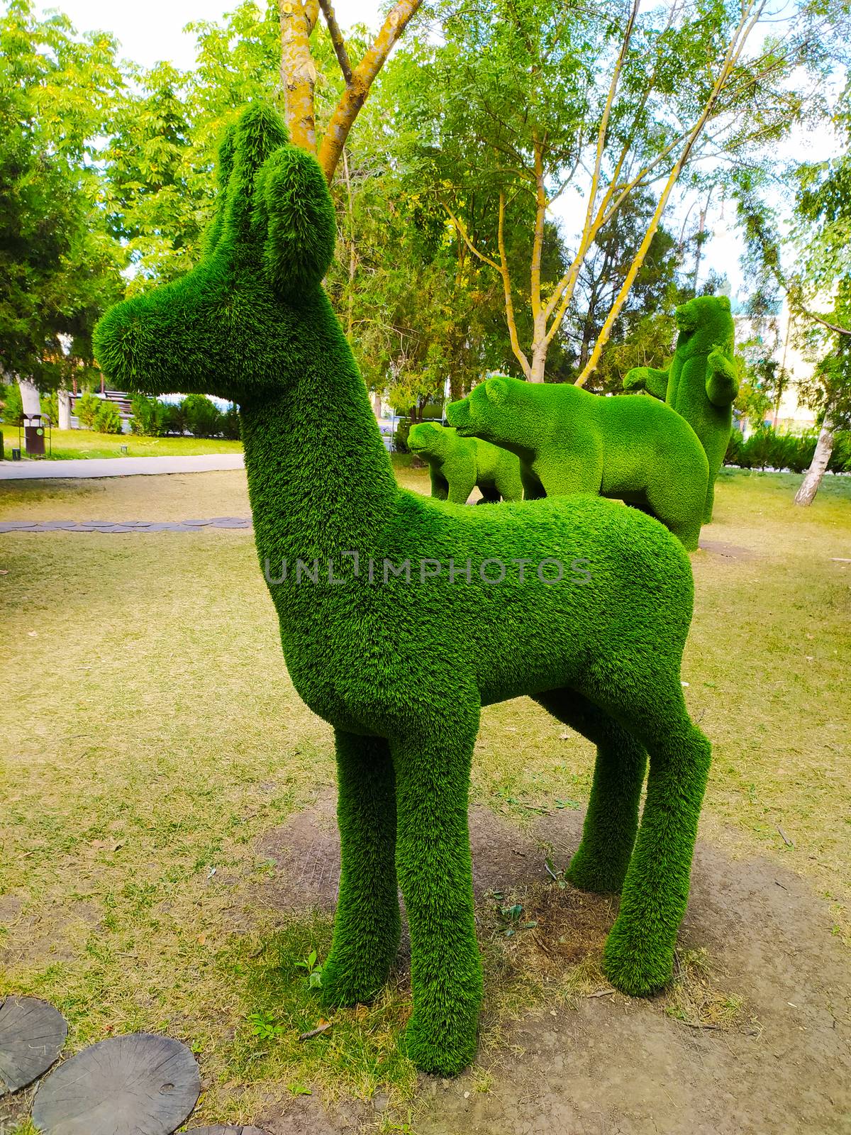 Sculpture of a deer in profile in a green Park against a background of trees.