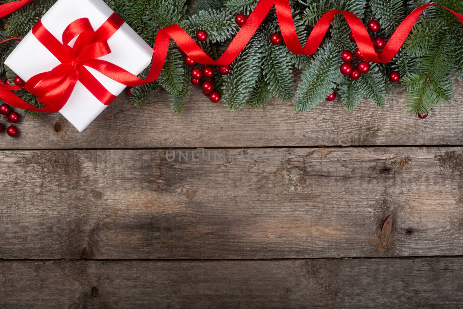 Christmas noble fir tree twigs and gift with red ribbon on wooden background with copy space for text