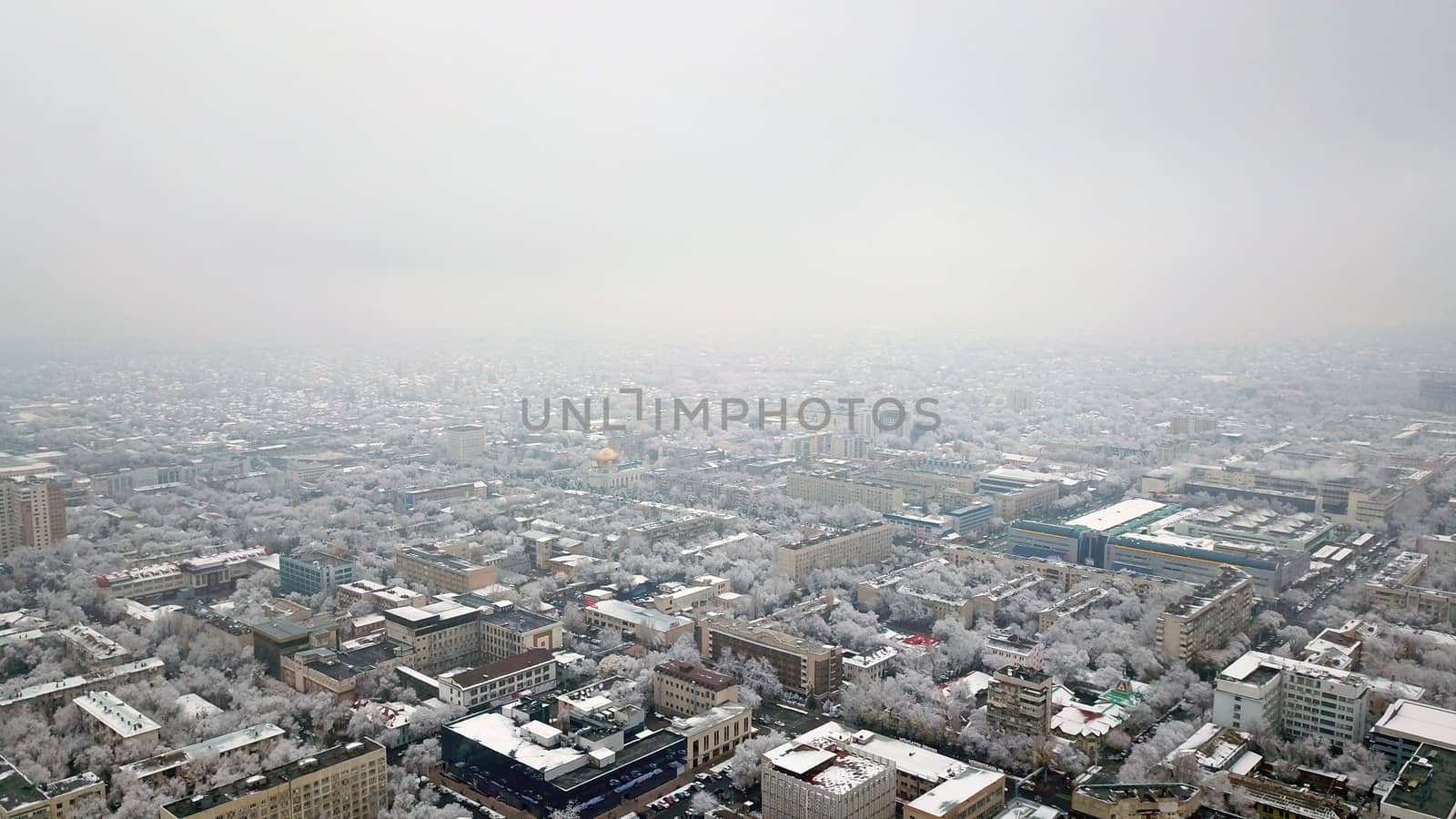 Top view through the clouds on the city of Almaty. Winter atmosphere, white trees, bushes, roofs of houses. Flying over the city. White clouds and light fog. Traffic of cars on roads. Through clouds.