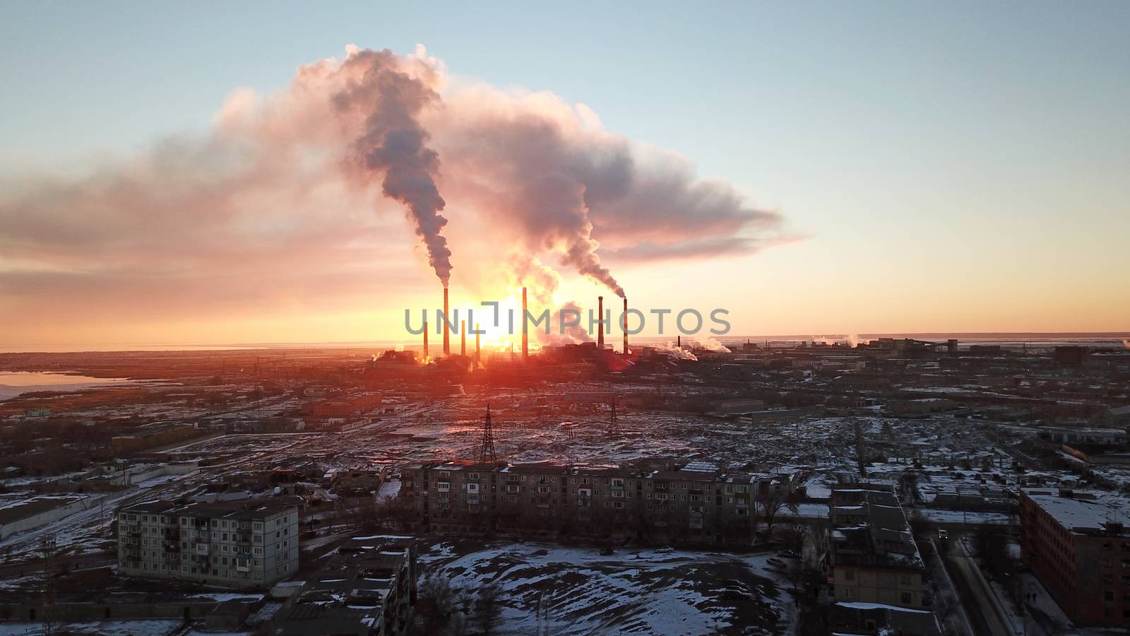 Epic sunset on the background of a Smoking factory. The red sun with bright rays goes beyond the pipe factories and smog. Shooting with the drone. View of part of the city, lake and industry. Red sky