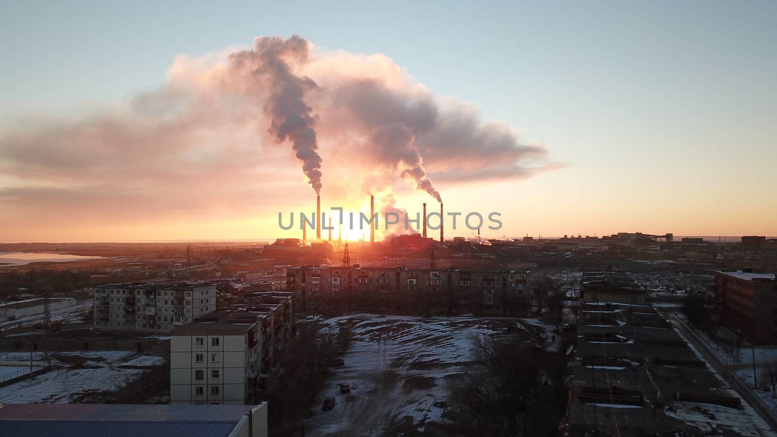 Epic sunset on the background of a Smoking factory. The red sun with bright rays goes beyond the pipe factories and smog. Shooting with the drone. View of part of the city, lake and industry. Red sky