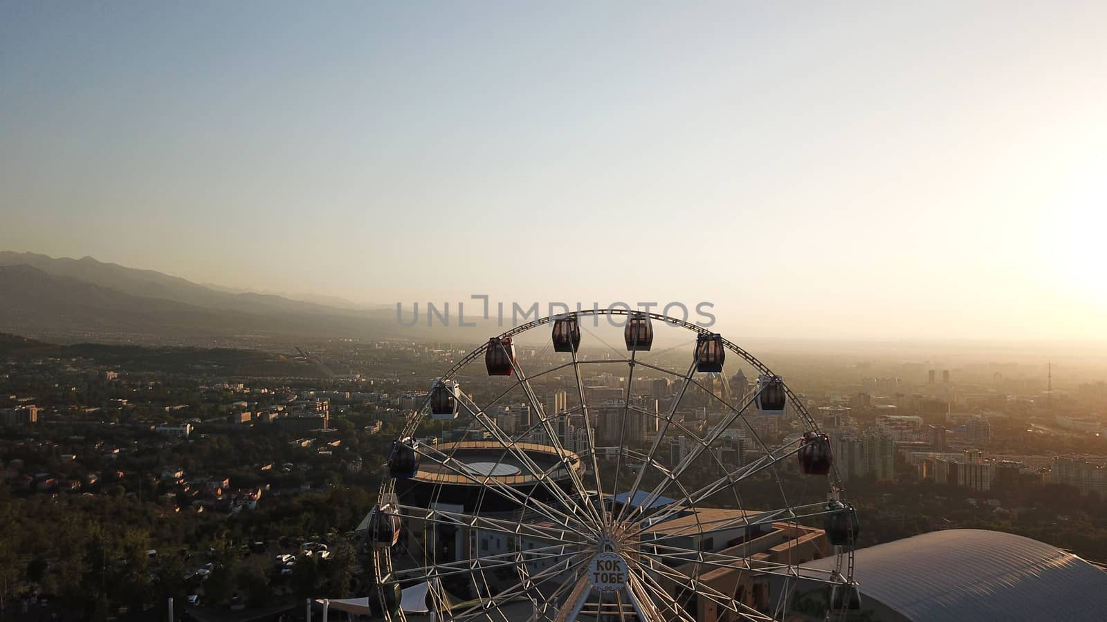 Ferris wheel on the green hill Kok Tobe at sunset by Passcal