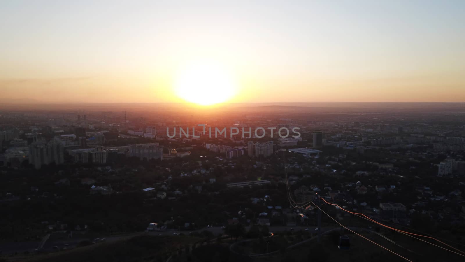 Red sunset over the city of Almaty. Clouds shimmer with different colors from yellow-red to blue. The city is plunged into darkness. Night falls. Lights are on, cars are driving. The view from the top