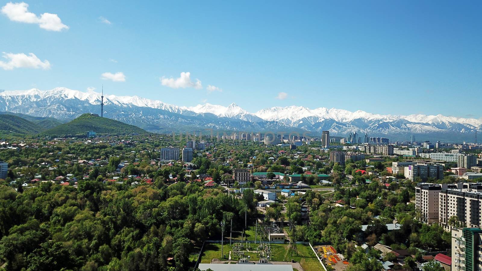 Almaty city Park with rides and a Ferris wheel. Completely green territory, lots of trees, grass, flowers. People are resting. View from a drone. Colored cabs of the Ferris wheel. Clean air and nature