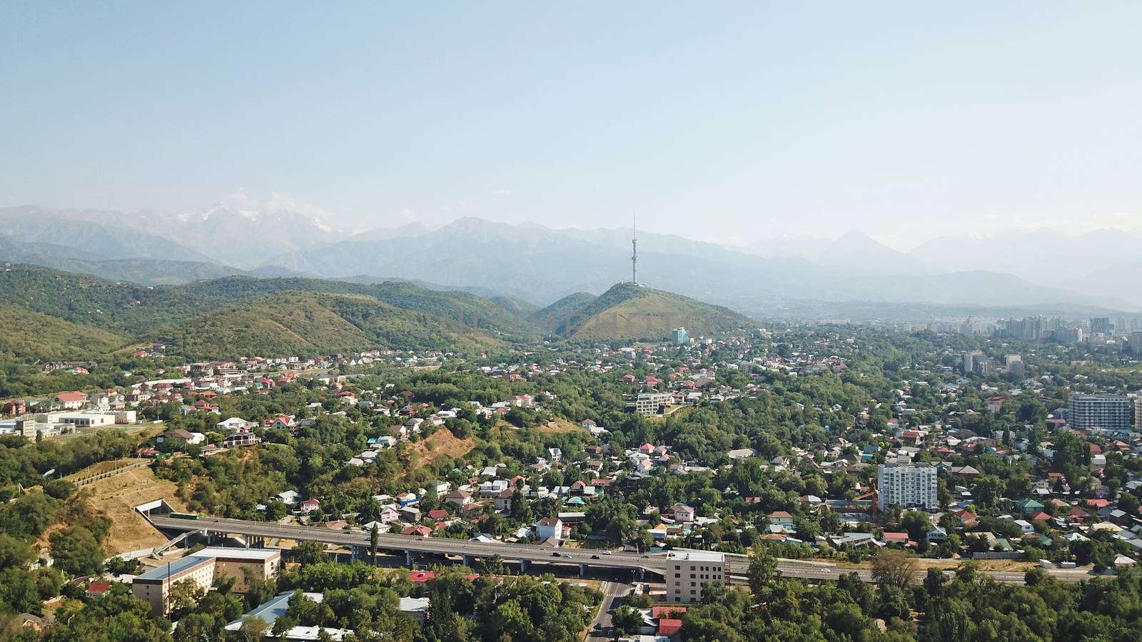 Almaty city Park with rides and a Ferris wheel. Completely green territory, lots of trees, grass, flowers. People are resting. View from a drone. Colored cabs of the Ferris wheel. Clean air and nature