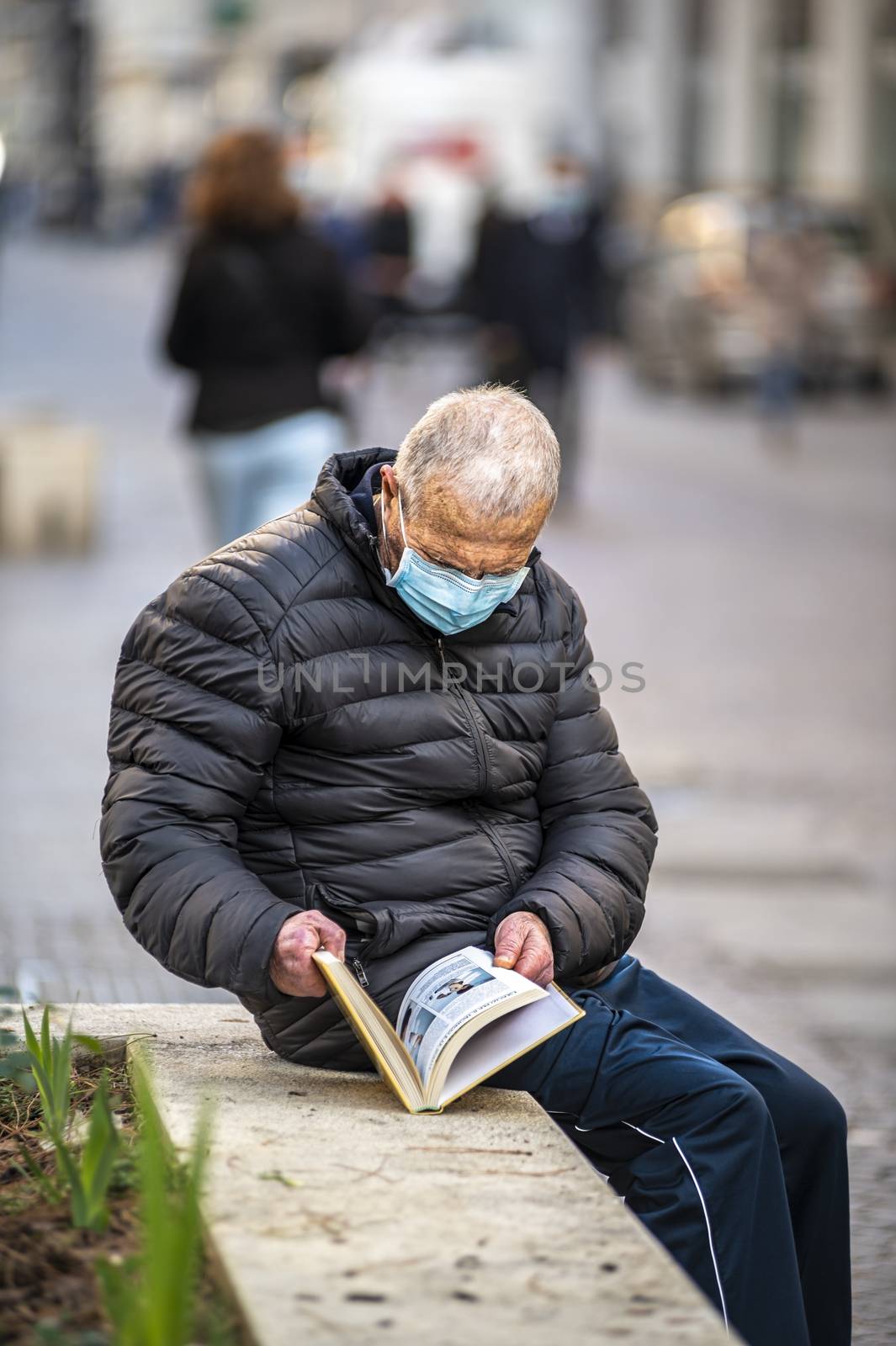 man with medical mask reads a book outdoors by carfedeph
