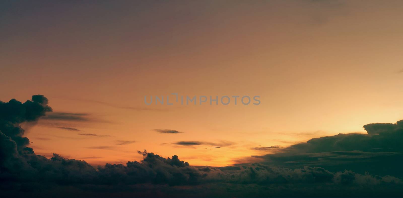 Beautiful golden sunset sky and dark clouds. Sky in the evening with yellow and orange light from the sun. Peaceful and tranquil background. Beauty in nature. Abstract background for inspiration quote