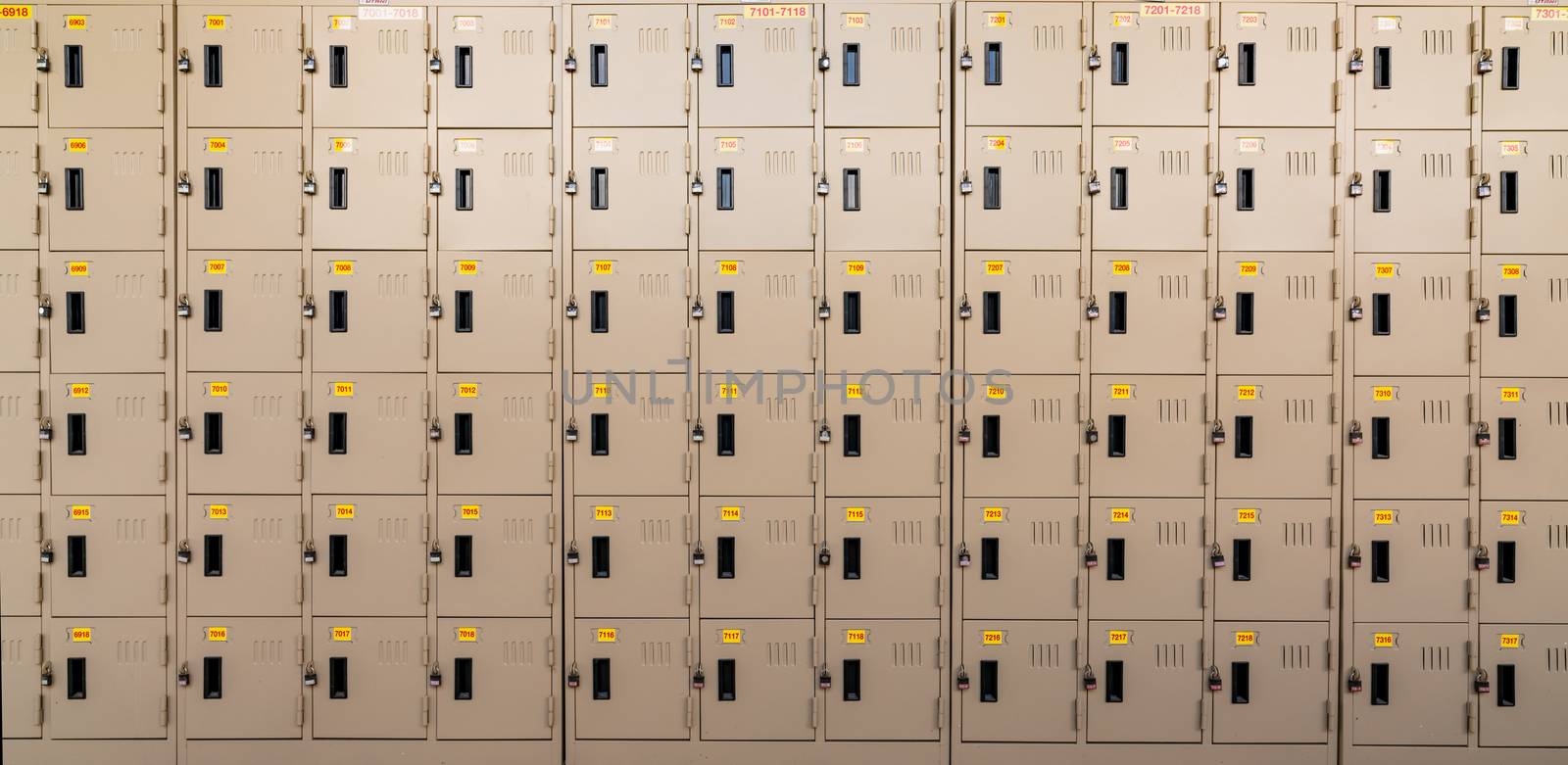 Closeup beige locker with lock and numbered yellow tags at locker room. Locker for safety and security storage. Row of locker with locked door background.