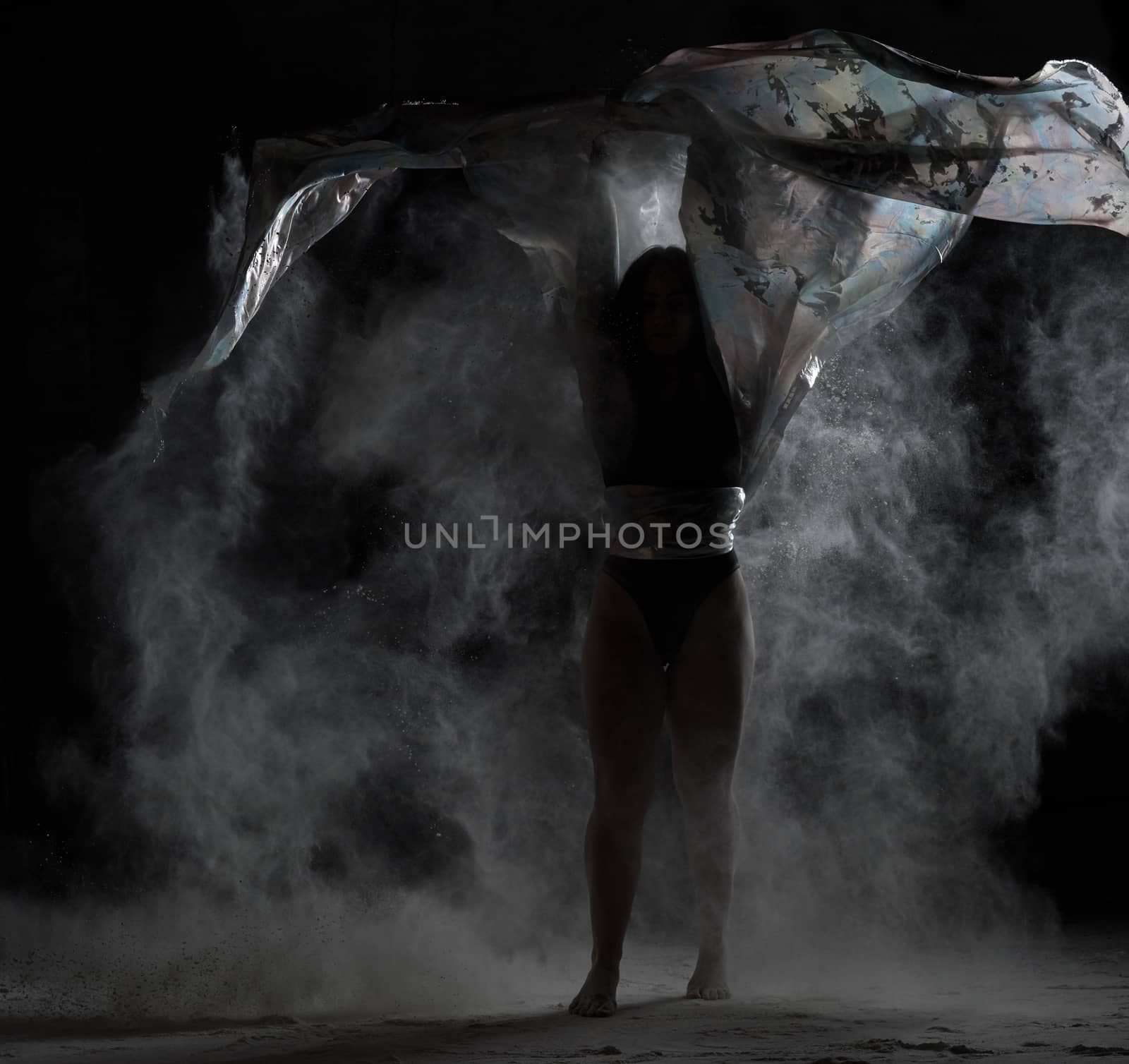 young athletic girl with long hair dances with a piece of cloth in a cloud of white flour, low key