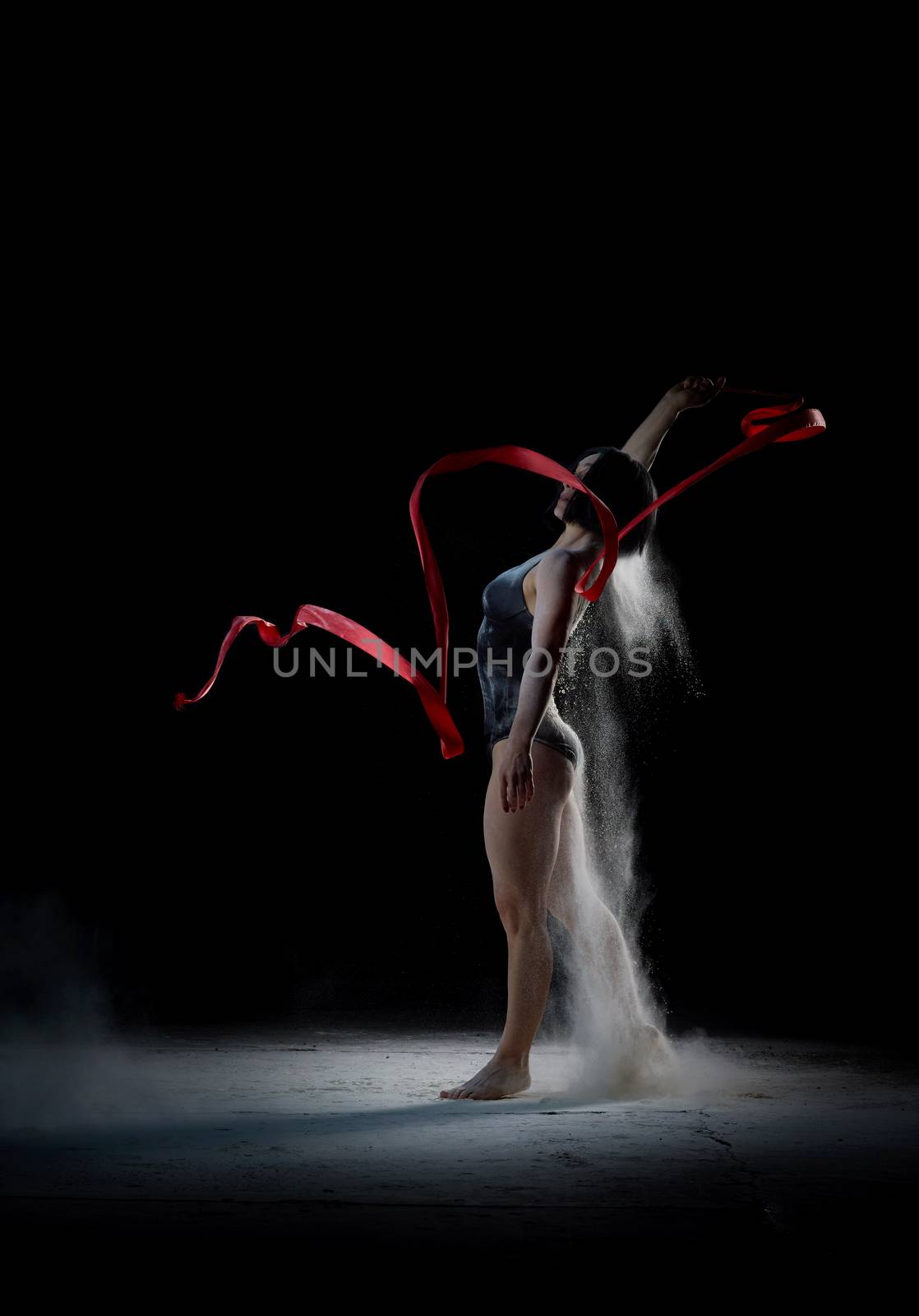 beautiful caucasian woman in a black bodysuit with a sports figure dancing with red ribbon on a black background, explosion and expression in motion