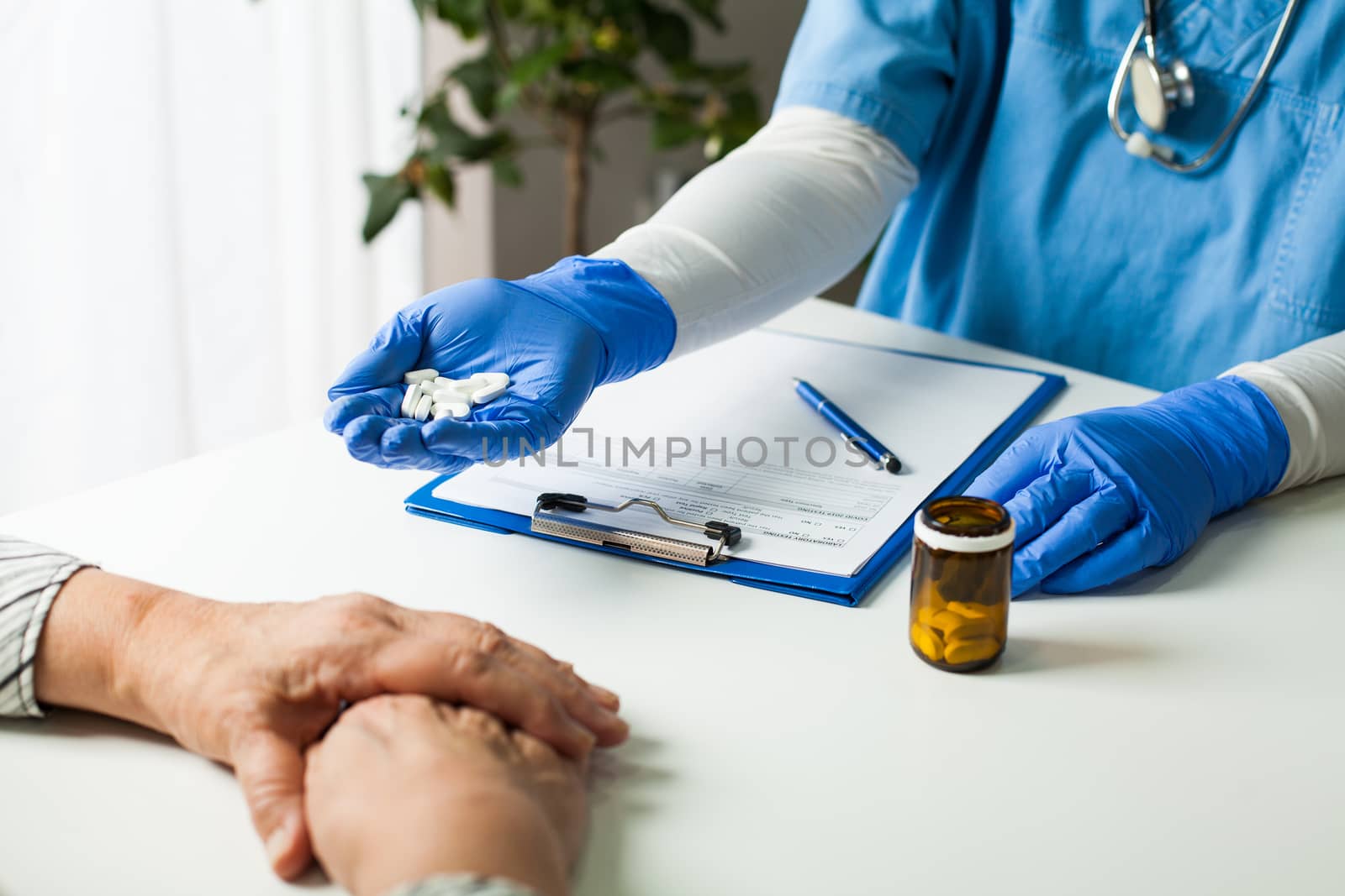 NHS GP UK doctor wearing blue protective latex gloves holding a handful of white pills,handing it over to elderly female senior patient,remedy & medication therapy for treating virus disease symptoms