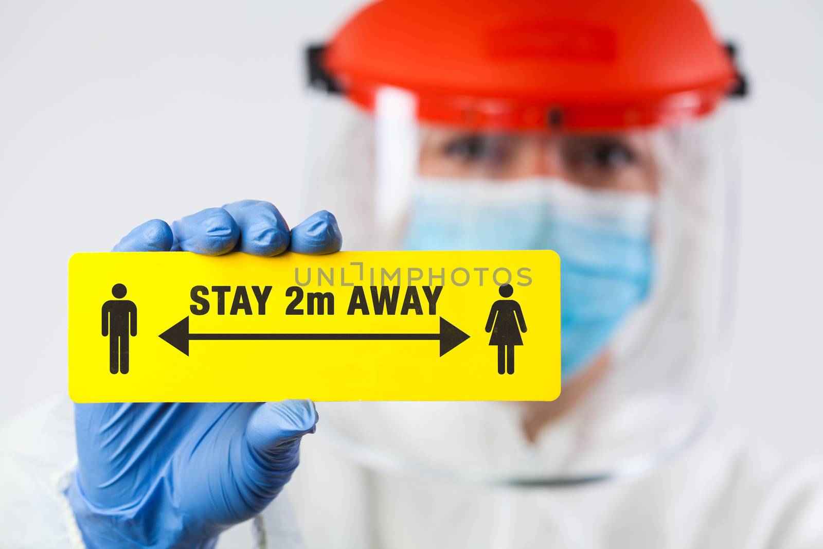 Medical worker in personal protective equipment holding yellow "STAY 2m AWAY" sign,social physical distancing to prevent and stop spread of viruses and infections,Coronavirus COVID-19 global pandemic