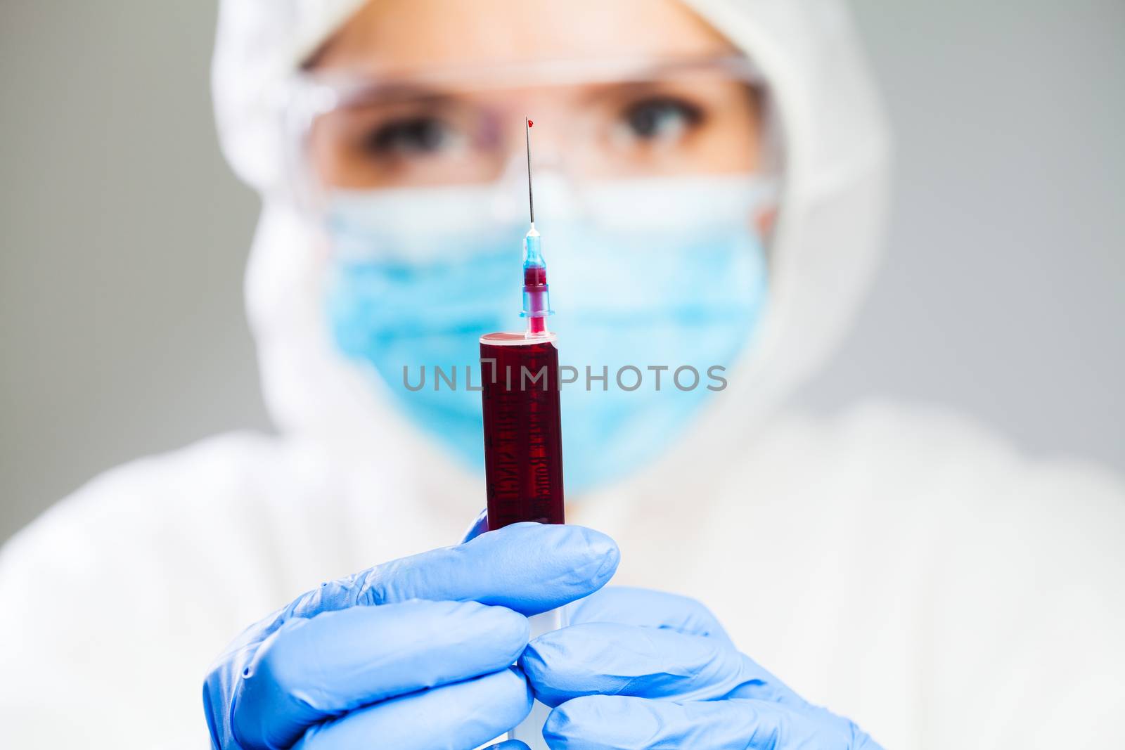 Doctor or lab scientist in personal protective equipment holding syringe jab full of blood plasma,focus on single drop dripping out of the needle tip,healthcare cure treatment and research for vaccine