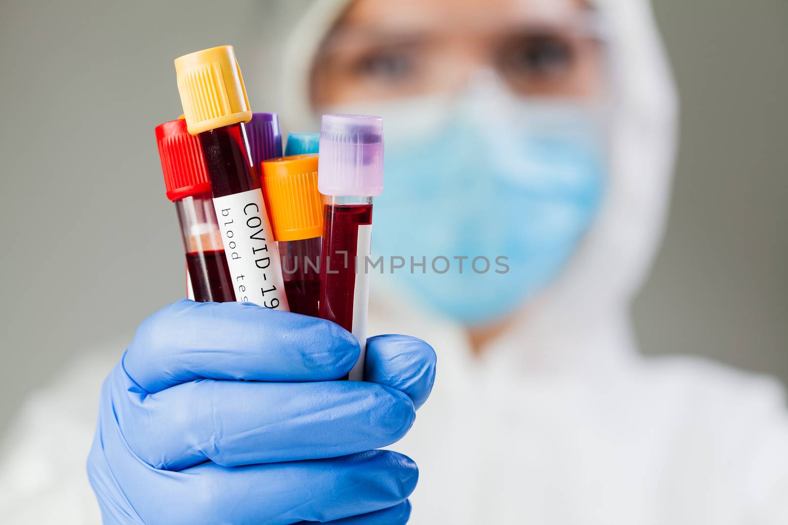 Lab scientist or medical technologist wearing hazmat protective suit and mask holding test tube vacutainers, Coronavirus patient blood sample, COVID-19 virus disease PCR DNA analysis visualization