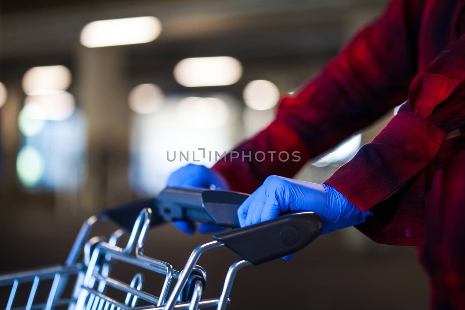 Person wearing blue protective surgical latex rubber gloves pushing shopping cart trolley, stocking supplies, panic buying and hoarding due to global Coronavirus COVID-19 pandemic crisis outbreak