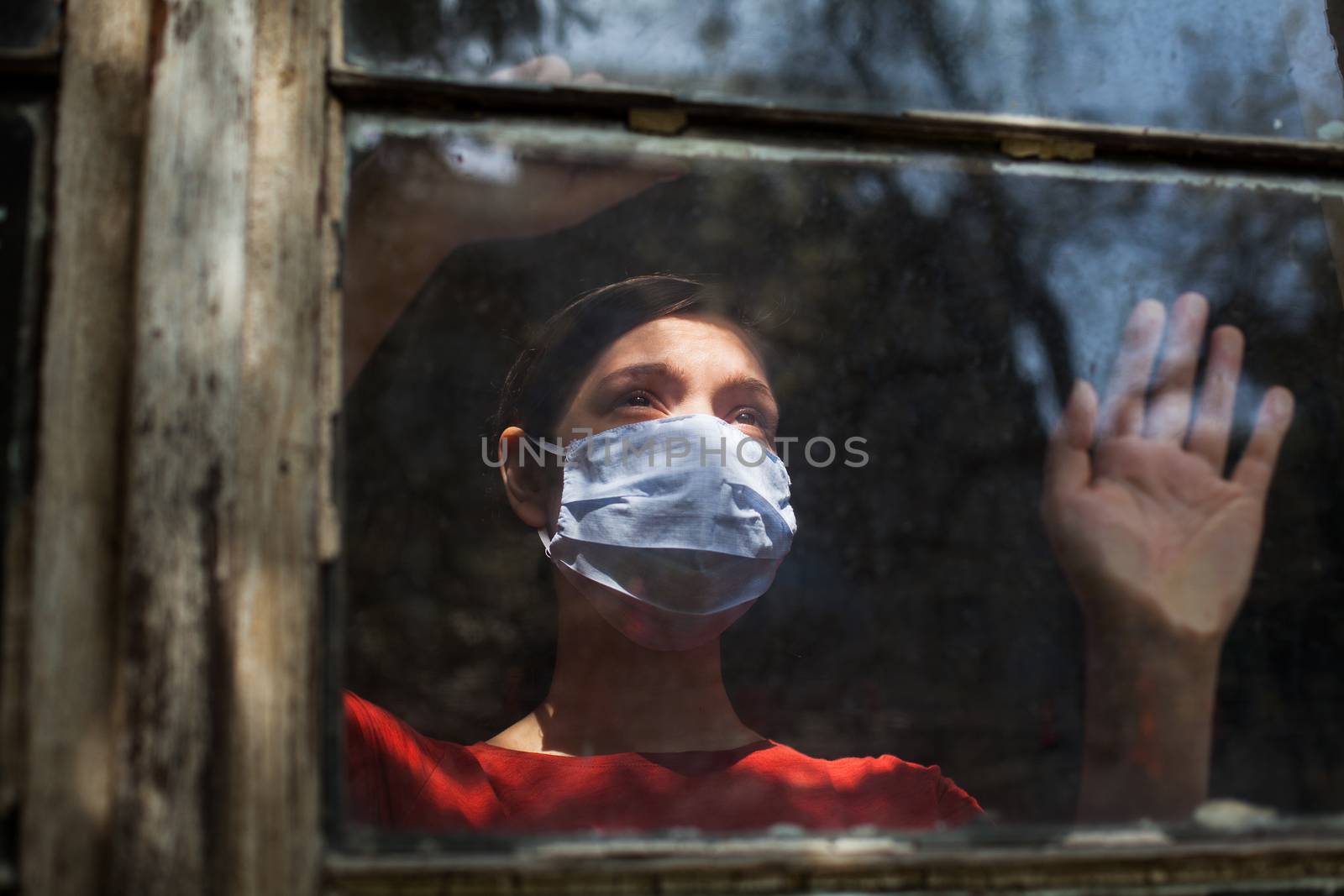 Sad depressed anxious young woman wearing protective medical mask looking outside the window, Coronavirus Covid-19 virus disease pandemic, self isolation quarantine lockdown, stay at home safe concept