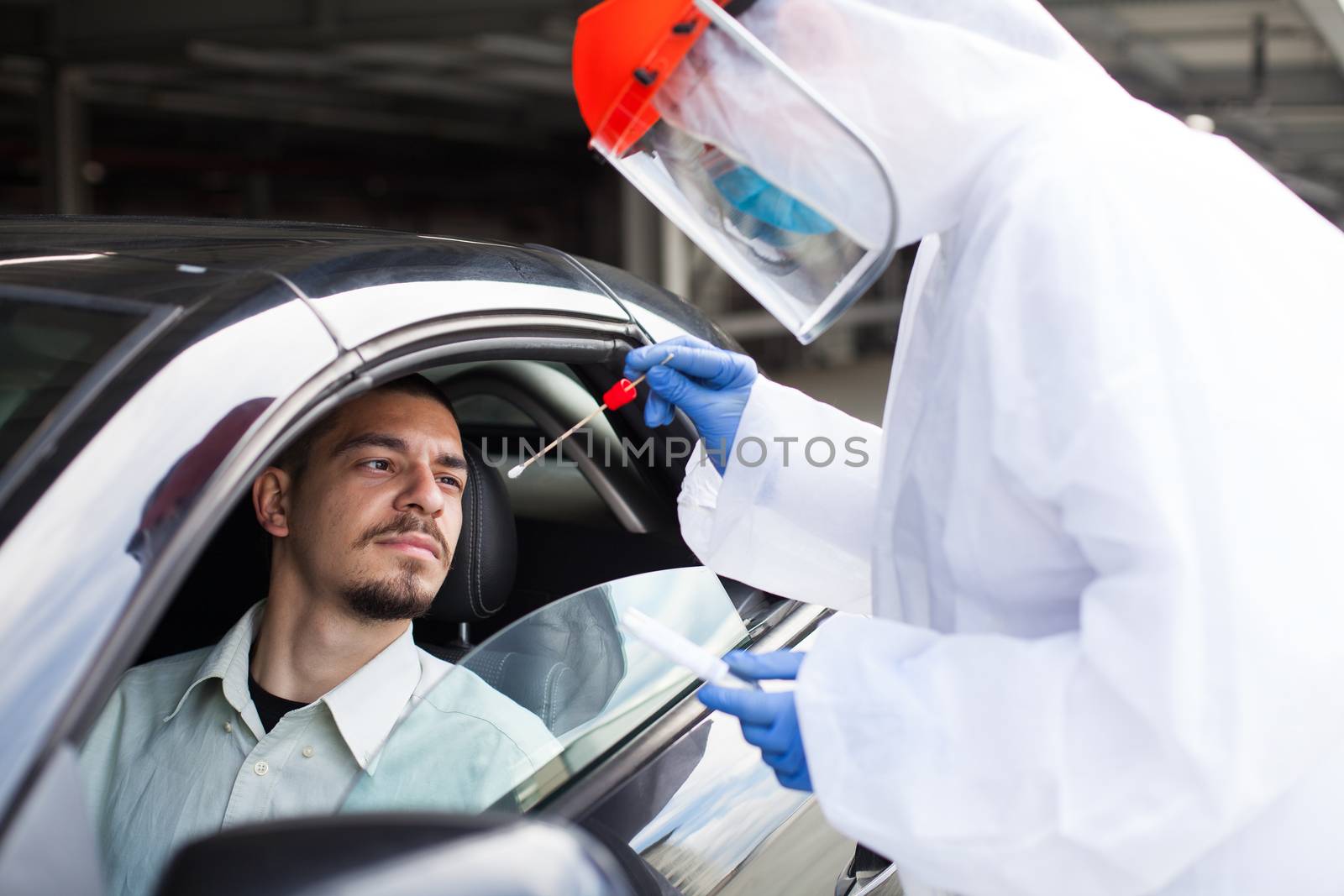 COVID-19 drive-thru rt-PCR detection,car checkpoint diagnostic,medical worker performing nasal swab specimen collection on young male driver through vehicle window,epidemiologist in PPE swabbing a guy