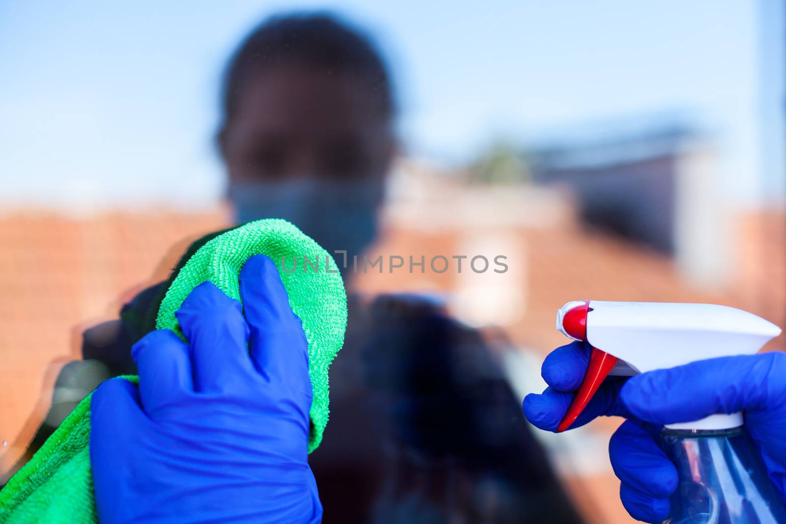 Female caucasian person in home isolation cleaning windows with cloth antibacterial sanitizing spray,wearing protective face mask and latex rubber gloves,Coronavirus COVID-19 pandemic virus diasease