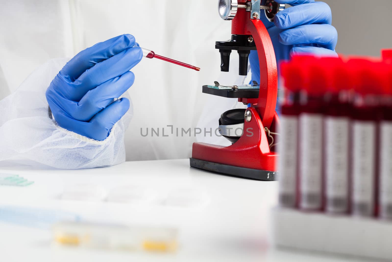 Medical technologist or lab scientist examining Coronavirus patient specimen,placing blood sample under microscope,analysis and research for potential COVID-19 vaccine cure