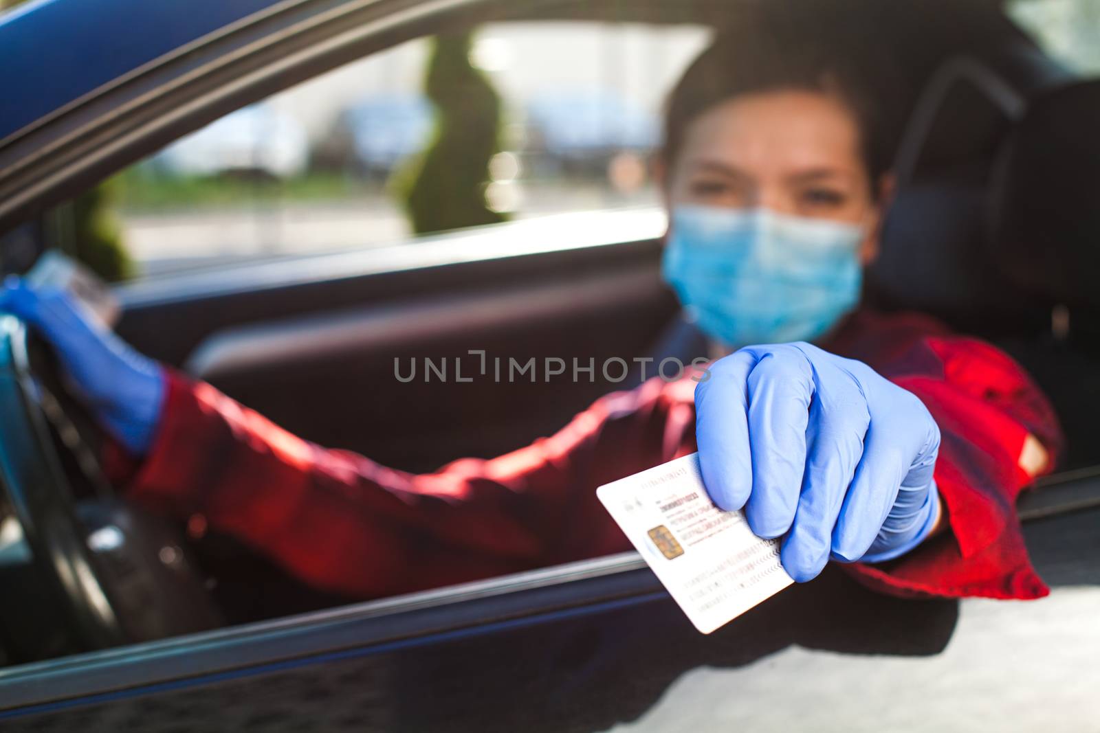 Young female driver showing Coronavirus health card or immunity passport,proof that a person has developed resilience,COVID-19 risk free certificate,hand holding identification through car window